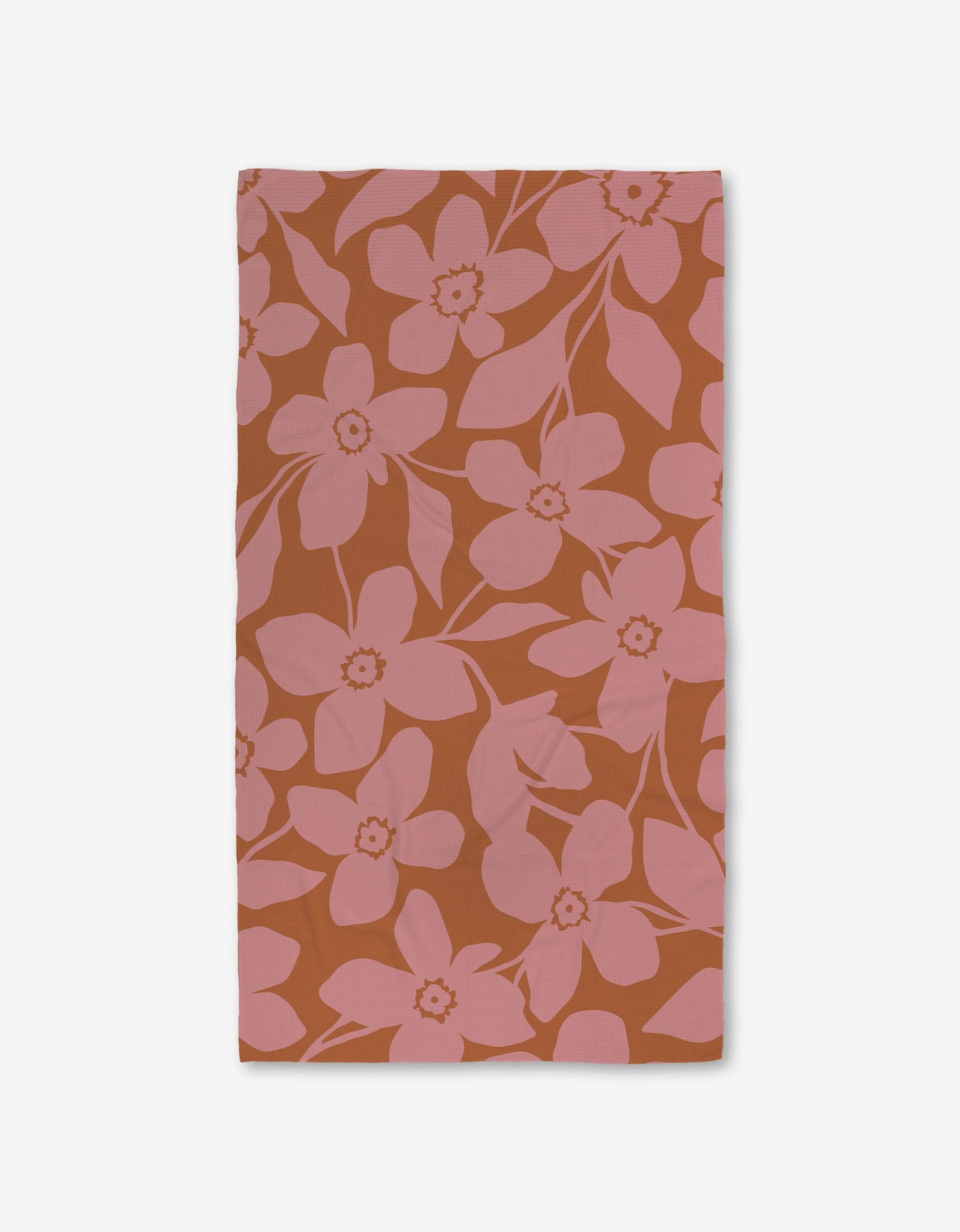 The GEOMETRY Big Fuchsia Flowers rectangular cloth napkin showcases large pink blossoms and leaves on a burnt orange background, displayed flat on white, and crafted with ultra-absorbent Geoweave technology for enhanced function.