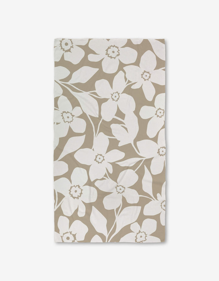 A GEOMETRY Big Tan Flowers Luxe Bath Towel, featuring a white floral pattern of large flowers and leaves made with Geoweave technology, is shown flat on a white background.