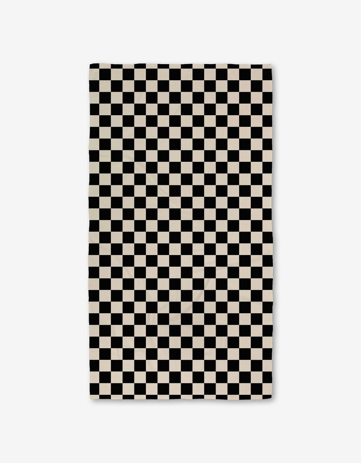 The GEOMETRY Checkered Luxe Bath Towel, featuring Geoweave technology and a black-and-white checkerboard pattern, offers an ultra-absorbent experience against a crisp white background.