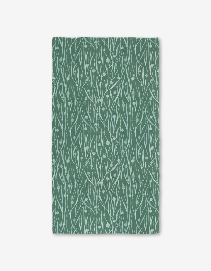 The Katie OShea Kelp Luxe Bath Towel is rectangular, green, and made from recycled materials. It features a white abstract botanical leaf-and-vine pattern and is photographed flat on a white background.