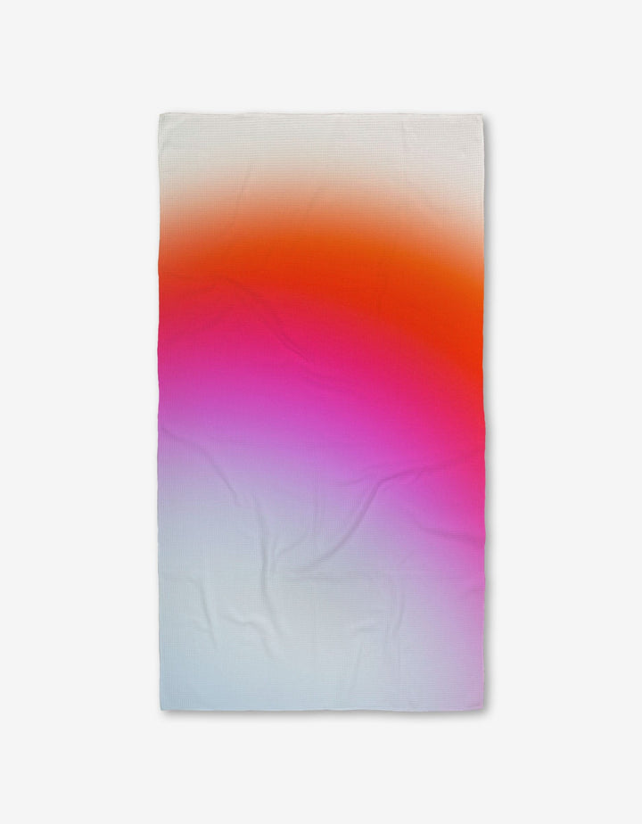 The GEOMETRY Lively Hue Bath Towel features a rectangular shape and a gradient design fading from white at the bottom to pink in the center and orange at the top, crafted with Geoweave technology and shown on a plain white background.
