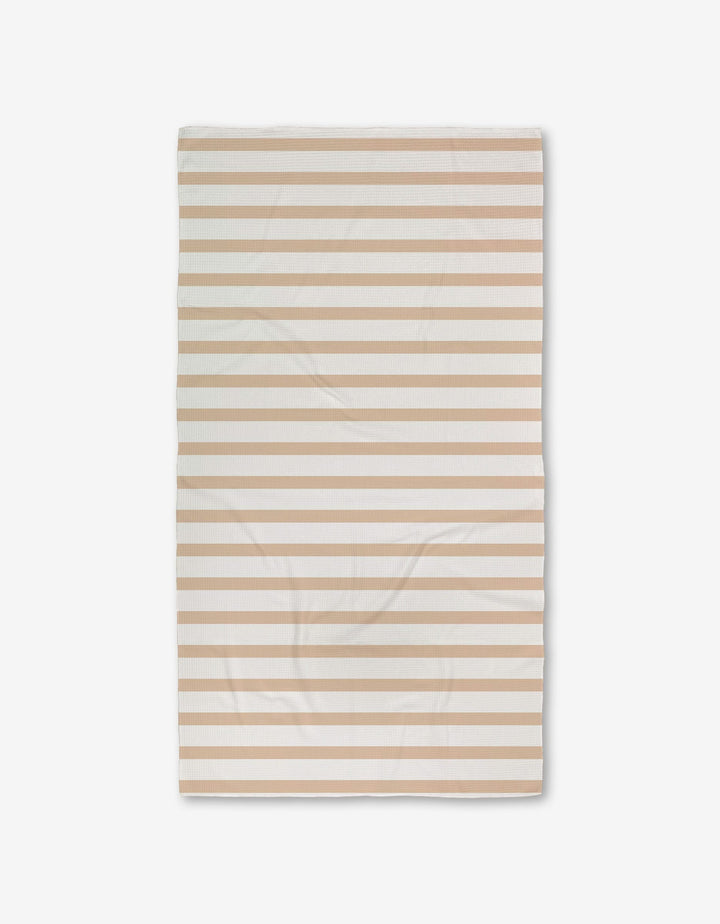 A rectangular GEOMETRY Sandalwood Stripes bath towel with horizontal beige and white stripes, featuring ultra-absorbent Geoweave technology, is laid flat on a white background and appears slightly wrinkled.