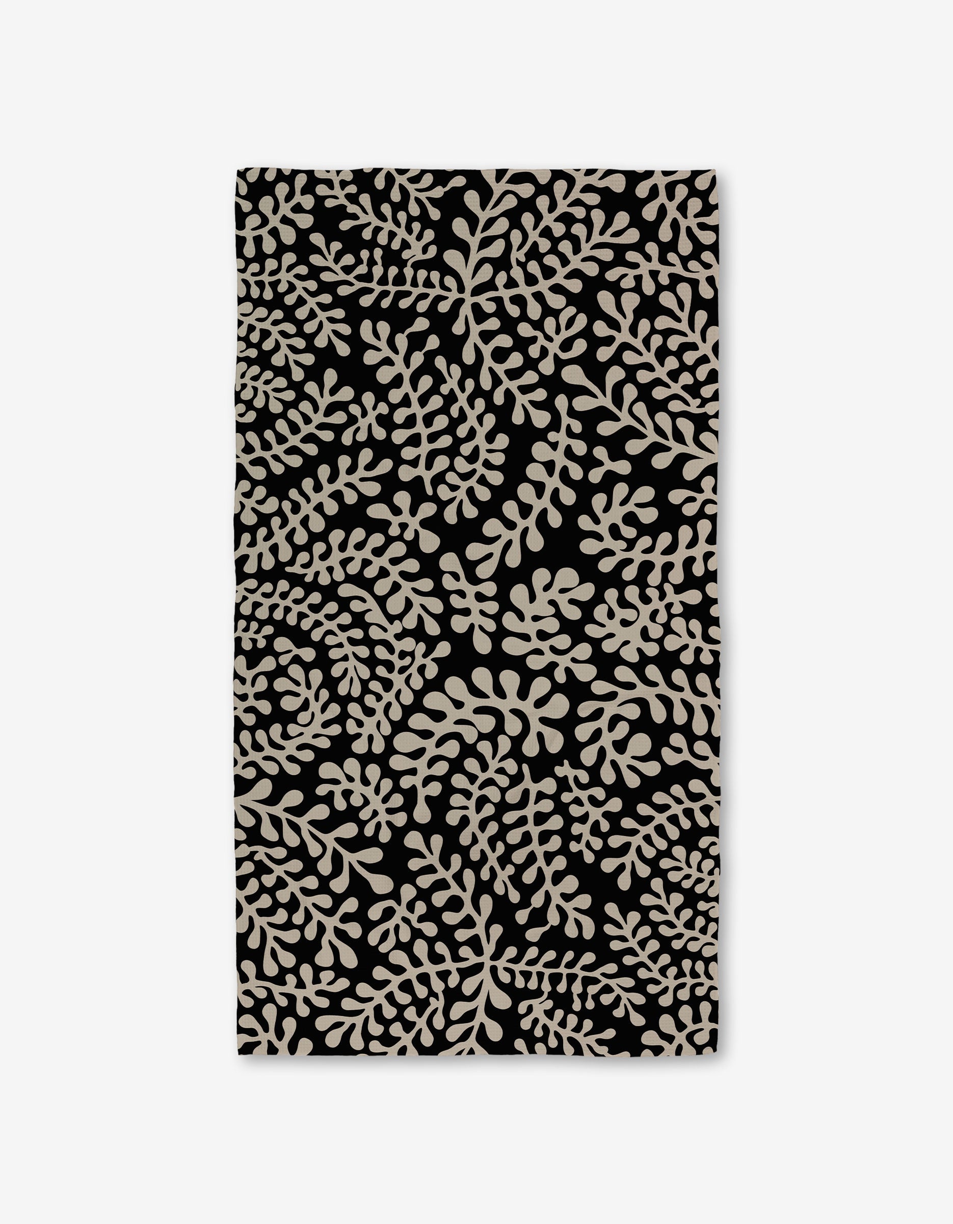 The GEOMETRY Tangled Luxe Bath Towel is rectangular and black, featuring a dense beige leafy pattern. Crafted with Geoweave technology, it offers superior absorbency and softness.