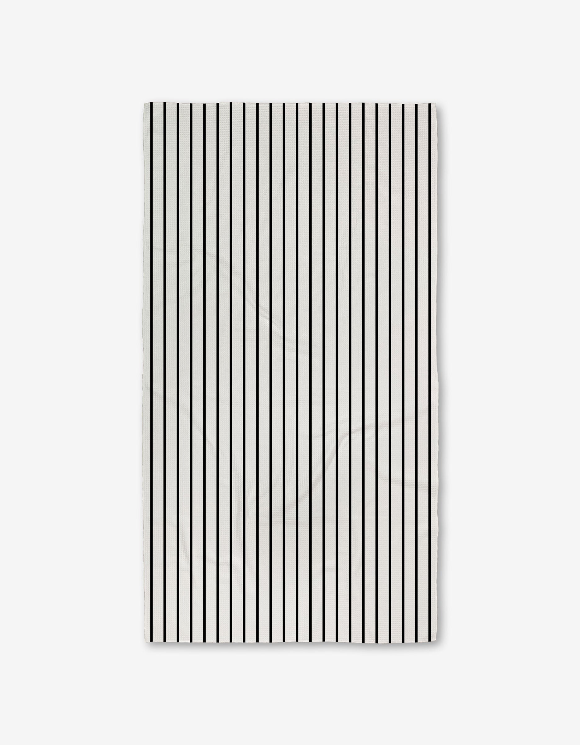 The White Linen towel by GEOMETRY is rectangular, white with evenly spaced vertical black stripes, crafted from ultra-absorbent recycled materials and shown against a plain light background.