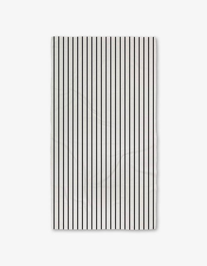 The White Linen towel by GEOMETRY is rectangular, white with evenly spaced vertical black stripes, crafted from ultra-absorbent recycled materials and shown against a plain light background.
