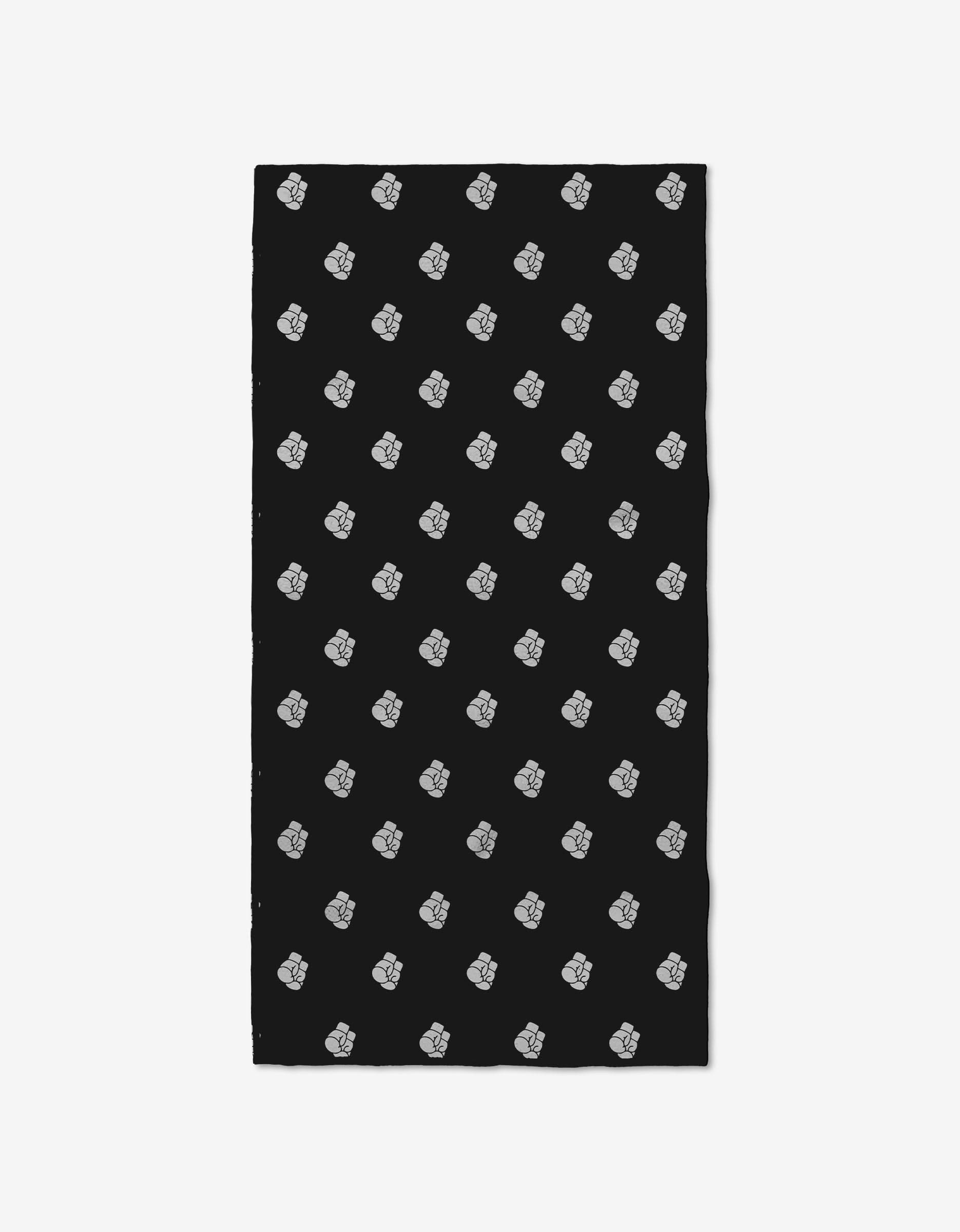 The Ashley Guarrasi Knock Out Fitness Towel is black, rectangular, and features a repeating diagonal pattern of small white cartoon skulls. Crafted from ultra-absorbent Geoweave fabric for top performance.