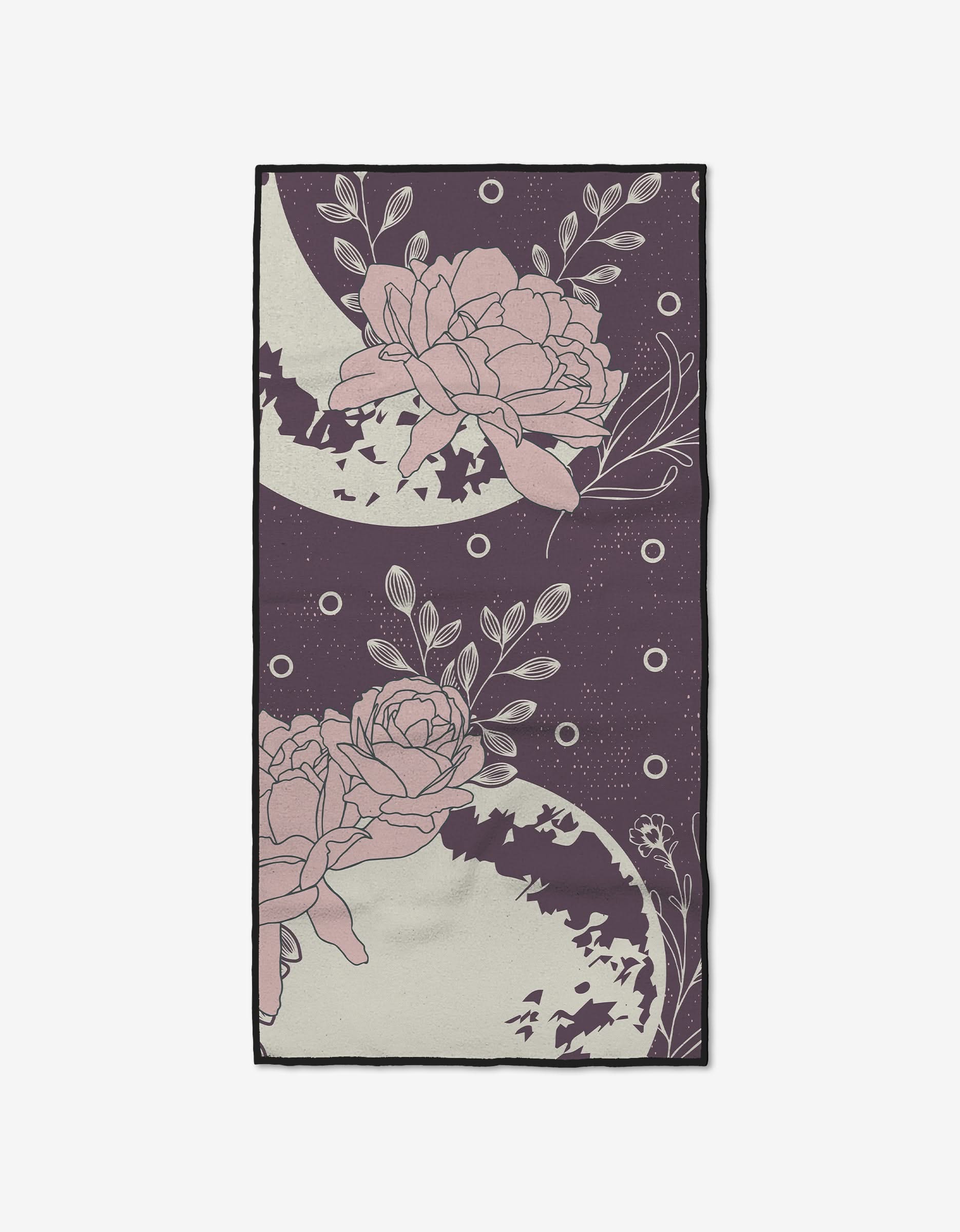 The Ashley Celena Midnight Garden is a rectangular, ultra-absorbent fitness towel with a dark purple background decorated with large pink flowers, leafy branches, crescent moons, and dots in an elegant pattern.