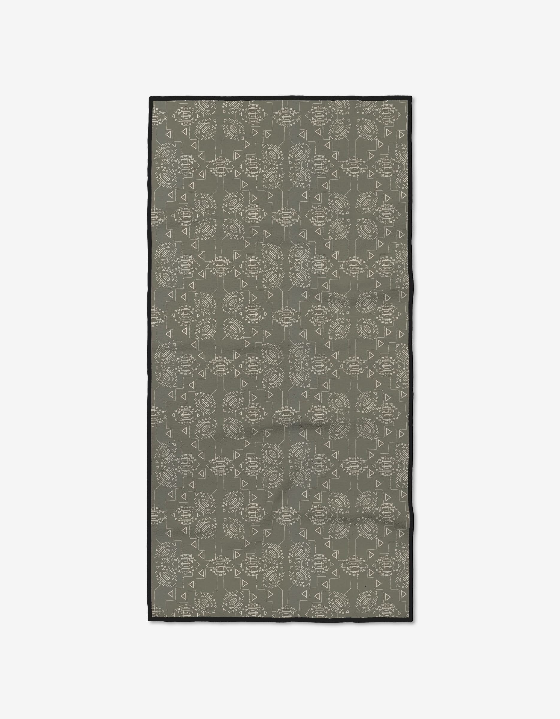 The Ash Cascade Mountain Bloom scarf is rectangular, crafted from recycled materials with a muted olive green base, beige geometric and floral designs, and a black border. It’s shown laid flat on a white background.