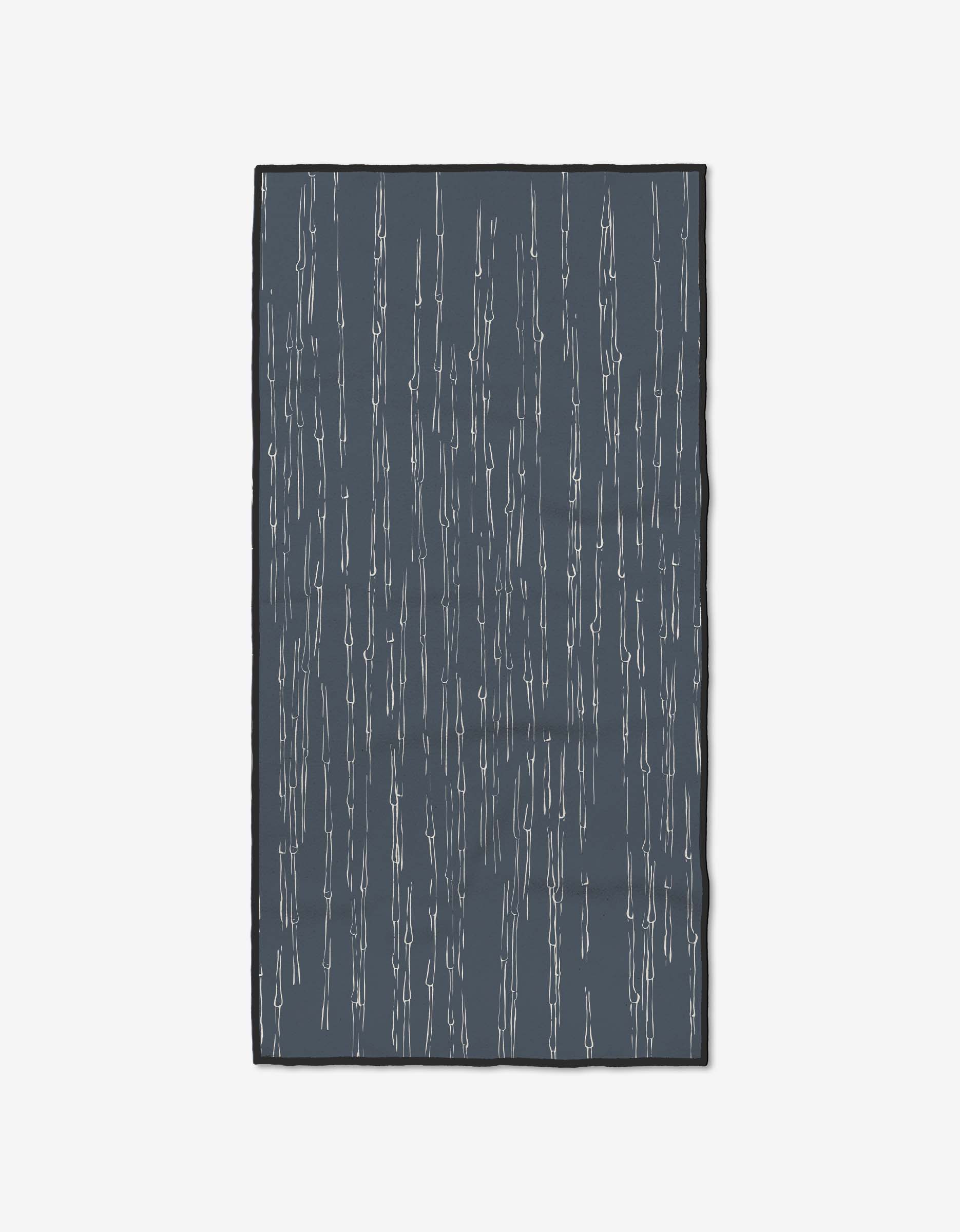 The GEOMETRY Stilts Midnight rug features an ultra-absorbent dark gray background with thin, uneven vertical white lines, resembling rain, against a plain white backdrop.