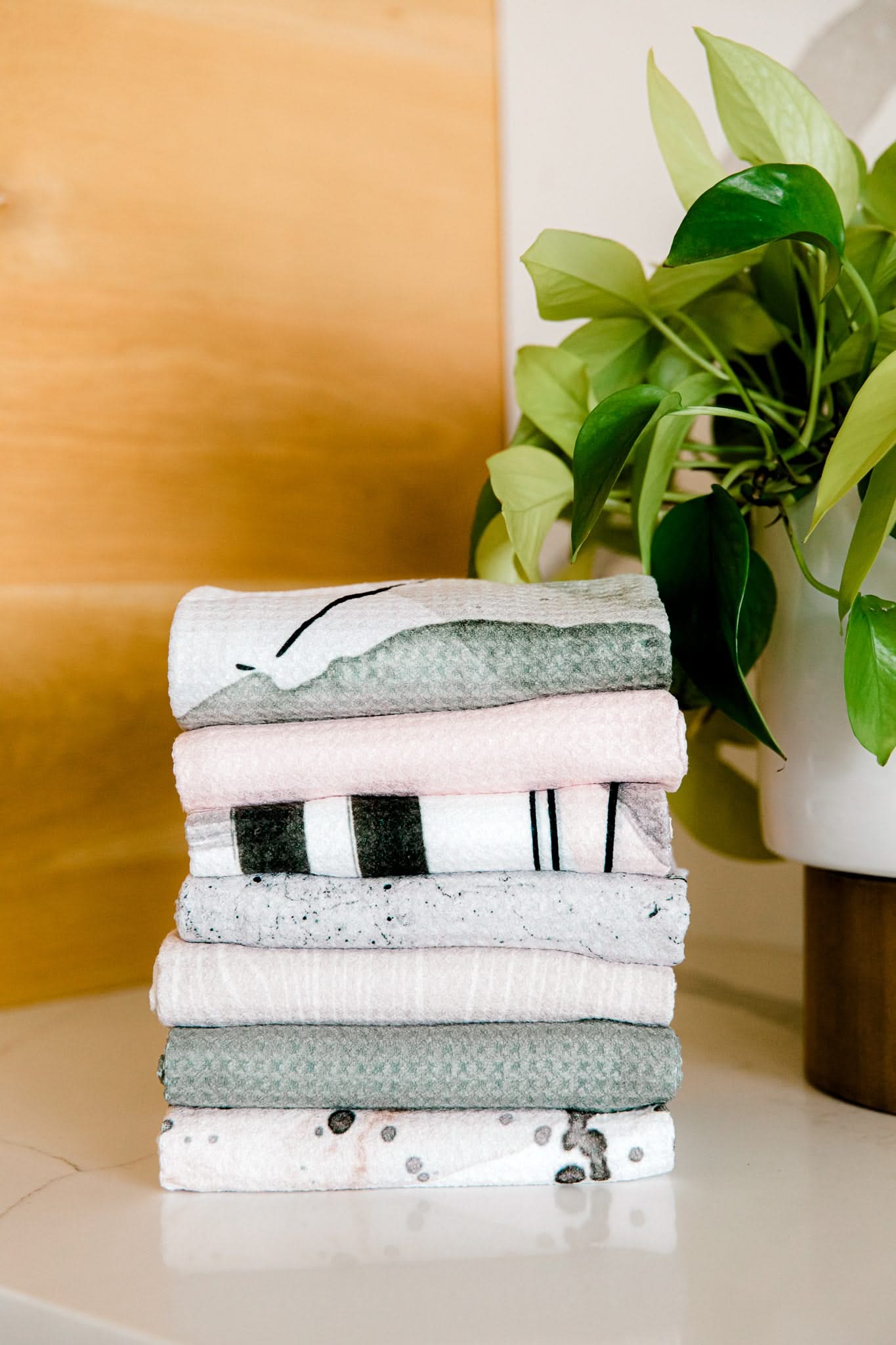 A neatly folded stack of Kailee Wright Hunter Green ultra-absorbent towels sits on a white countertop beside a leafy potted plant.