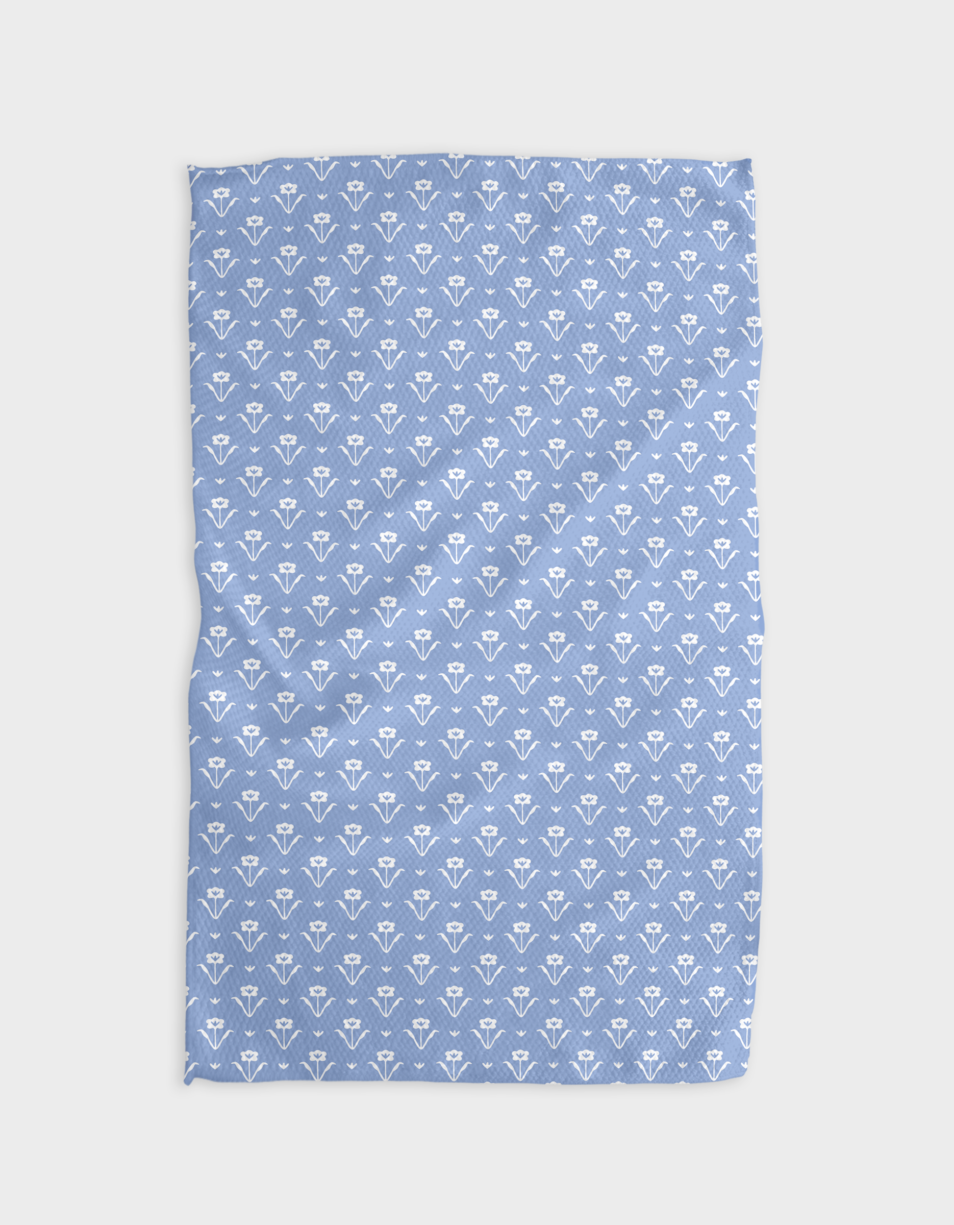 The Buy Guides Ladylike - French Blue tea towel, made from Geoweave fabric and adorned with a repeating pattern of small white tulip-like flowers, is laid flat with gentle wrinkles on a white background.