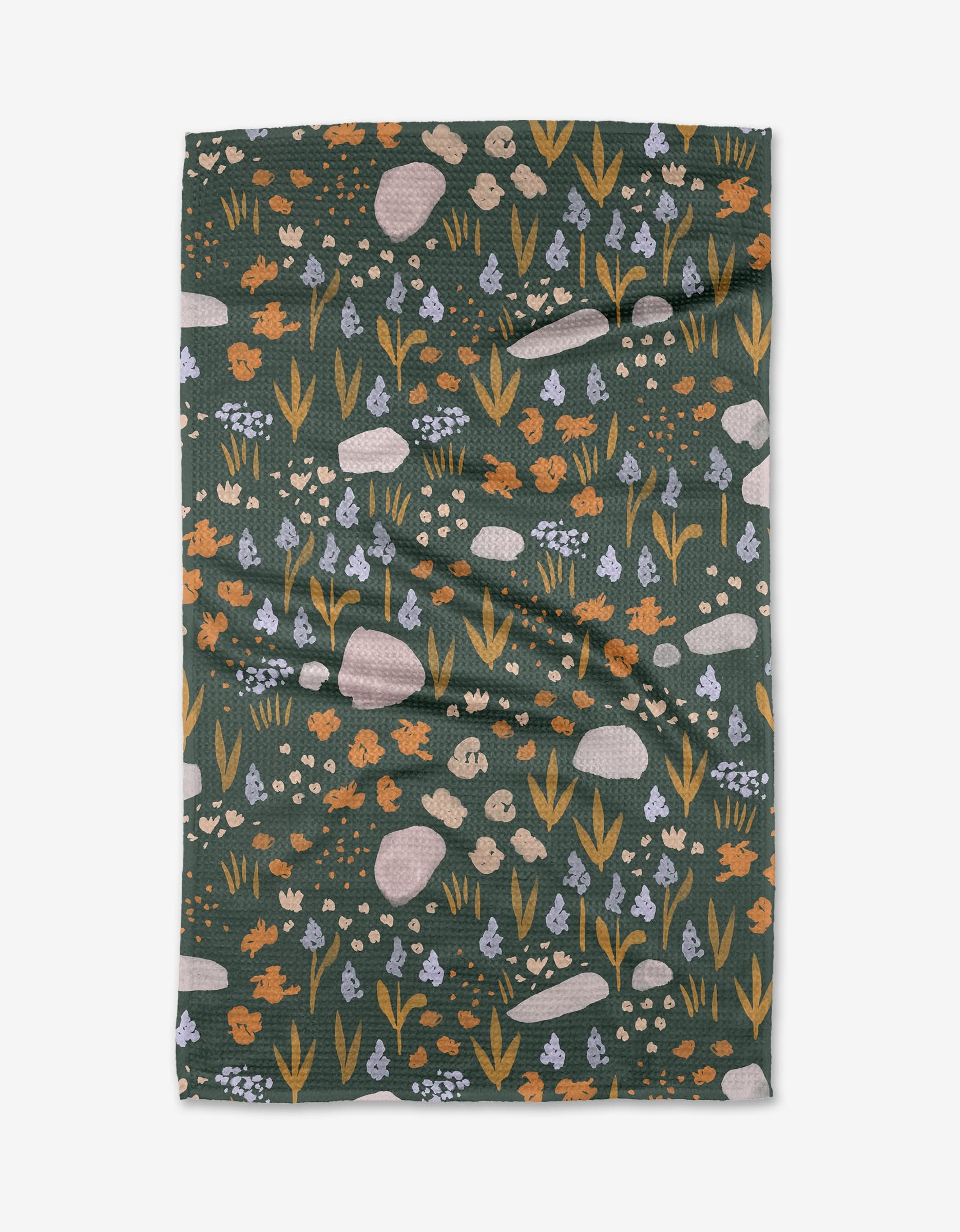 The Alpine Meadow Bold blanket by Mandy Arroyo is dark green, made from recycled materials, and features orange rabbits, tan mushrooms, rocks, and blue-white flowers in yellow-green grass. It is laid flat with a slightly wrinkled appearance.