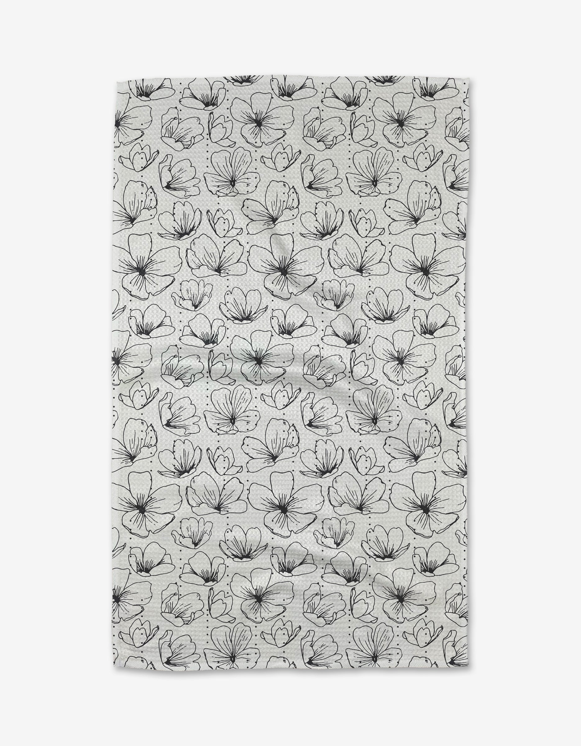 The Always Blooming tea towel by Rosa Kichline is rectangular, made from recycled materials, and showcases an all-over white surface with a repeating pattern of outlined black flowers and leaves.