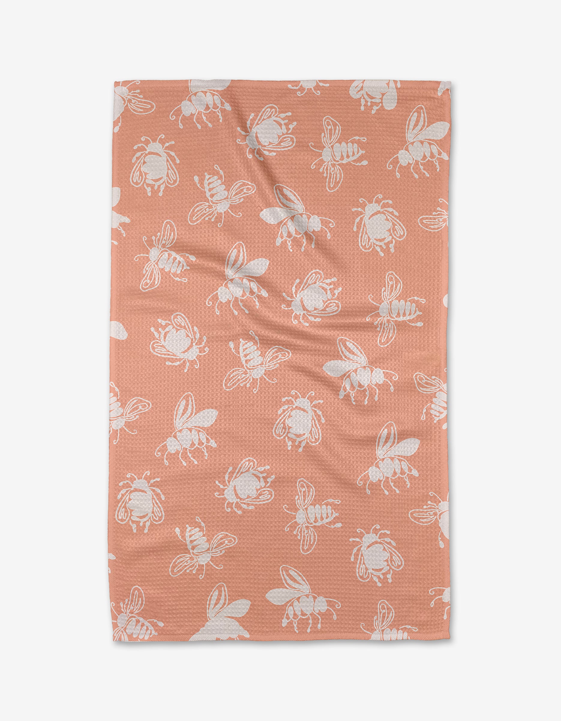 The Beelieve blanket by Sara Mari is peach-colored, made from recycled materials, and showcases a pattern of white bees in various positions evenly spread across its surface.