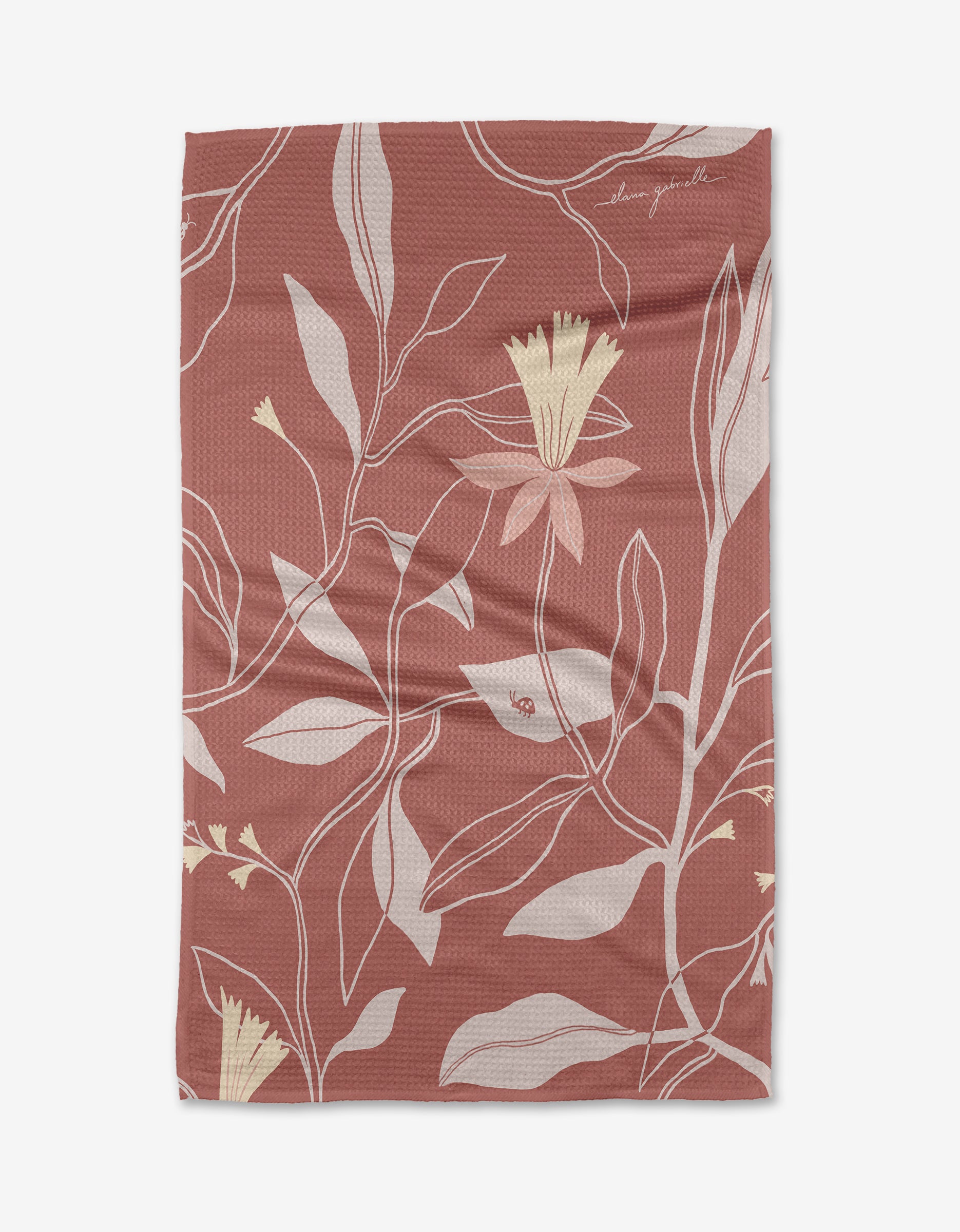 The Blooms Tea Towel by Elana Gabrielle features a rectangular shape, muted reddish-brown background, beige and yellow floral pattern with white line details, and is made from recycled materials for an eco-friendly touch.