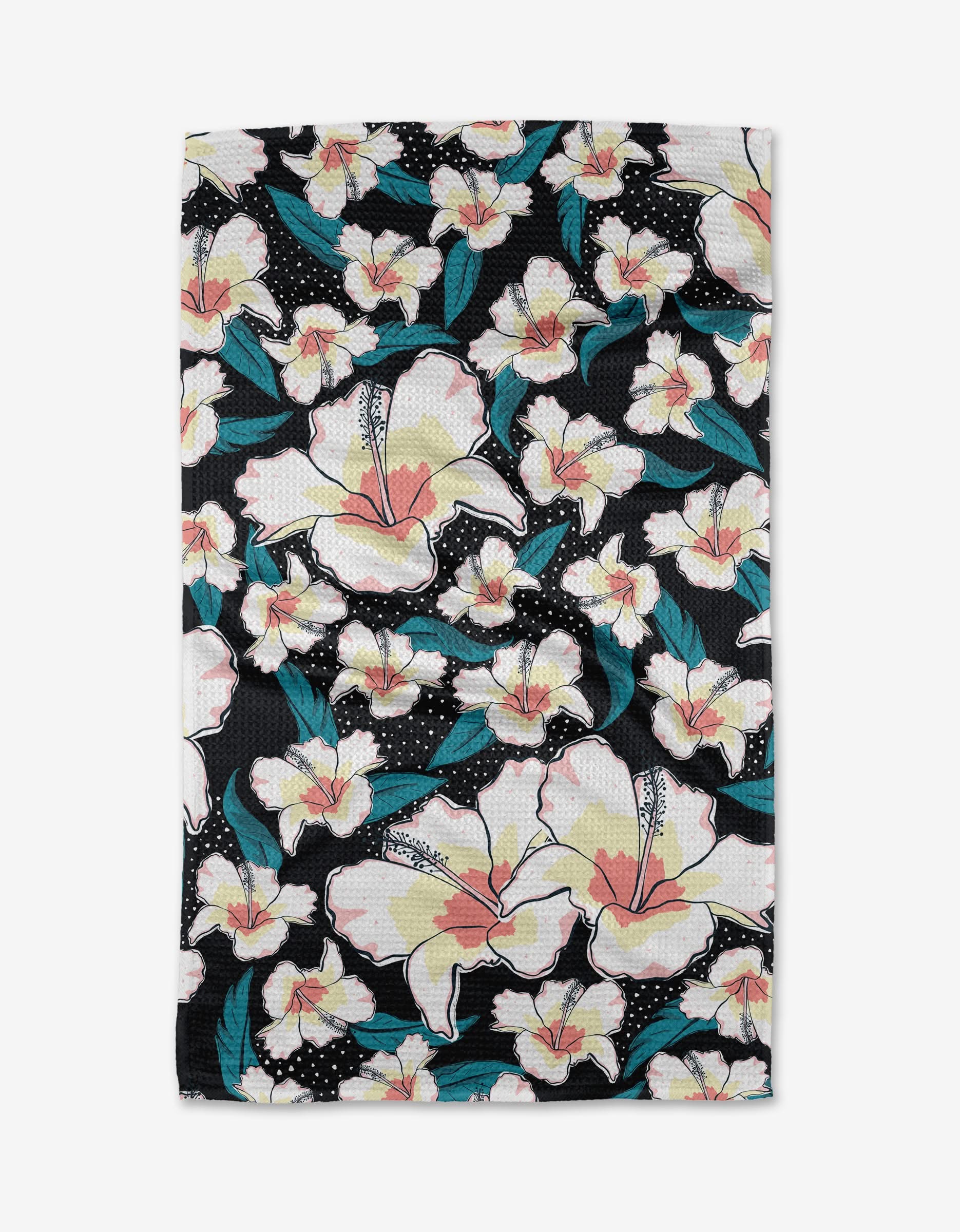 A neatly folded Cabo Cutie tea towel by Julianne Haness, rectangular and black, features a vibrant floral pattern with large white flowers, pink centers, teal leaves, and white dotted accents on a white background.