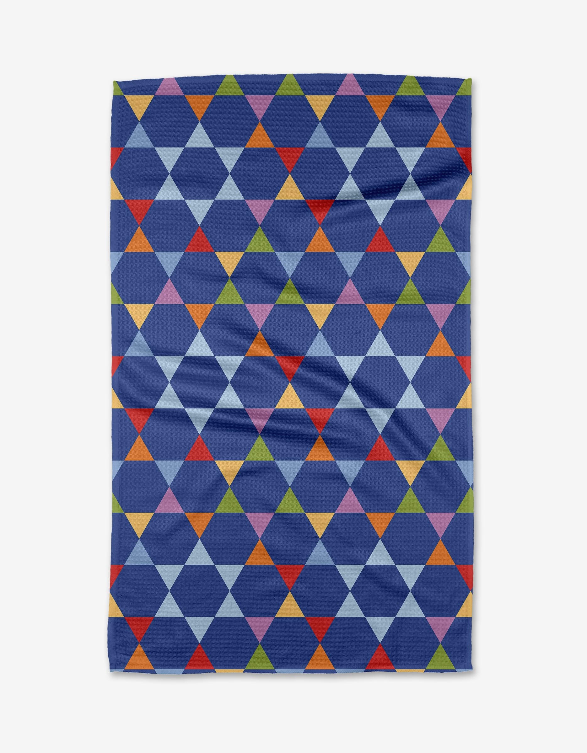 The Celebration tea towel by Mindfulnice is made from recycled materials and features a geometric tessellation of colorful red, orange, yellow, green, blue, and purple triangles on a dark blue background.