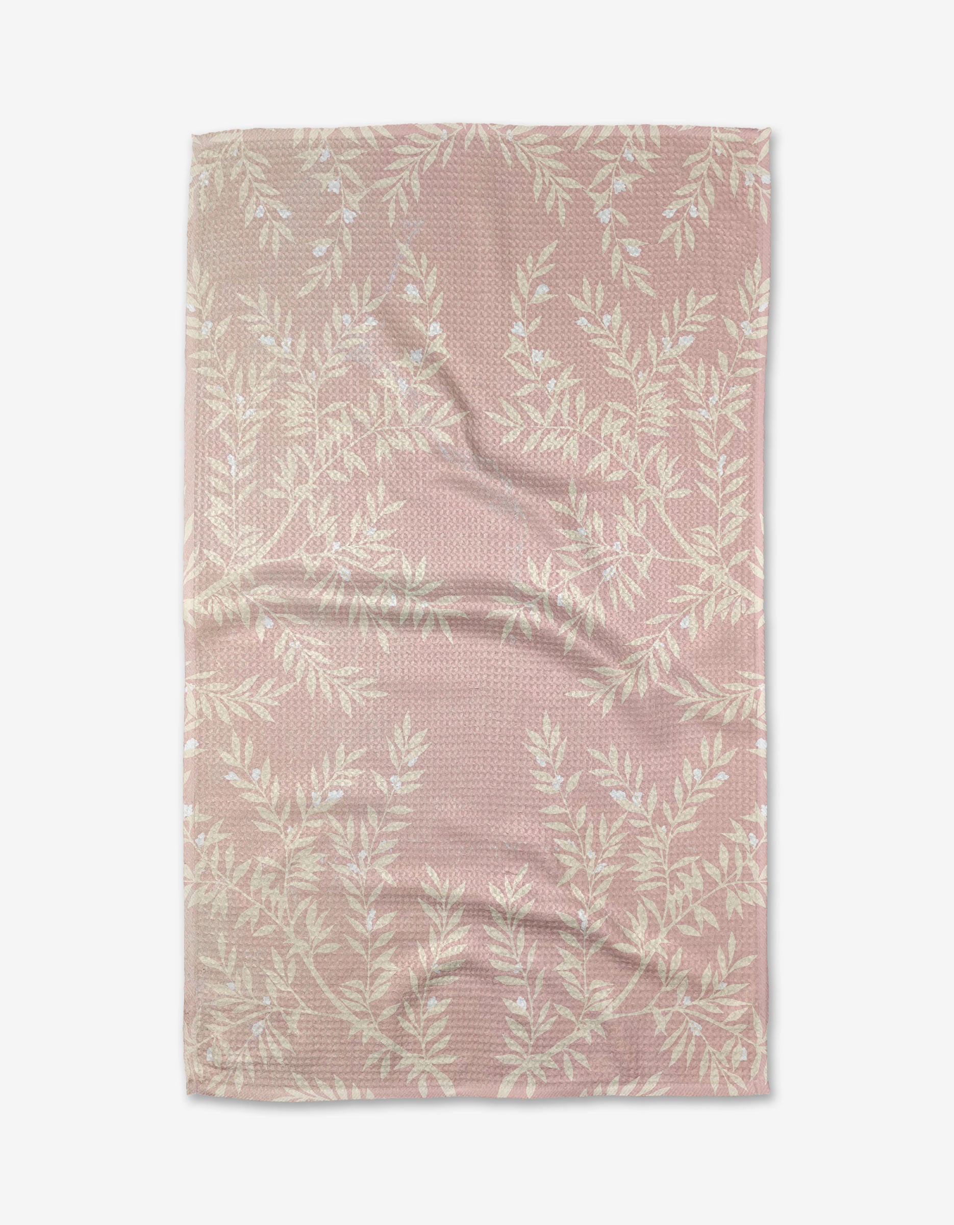 The Charlotte tea towel by Becki Owens features pink textured Geoweave™ fabric with a white leafy branch pattern, shown laid flat with visible creases and folds on a white background.