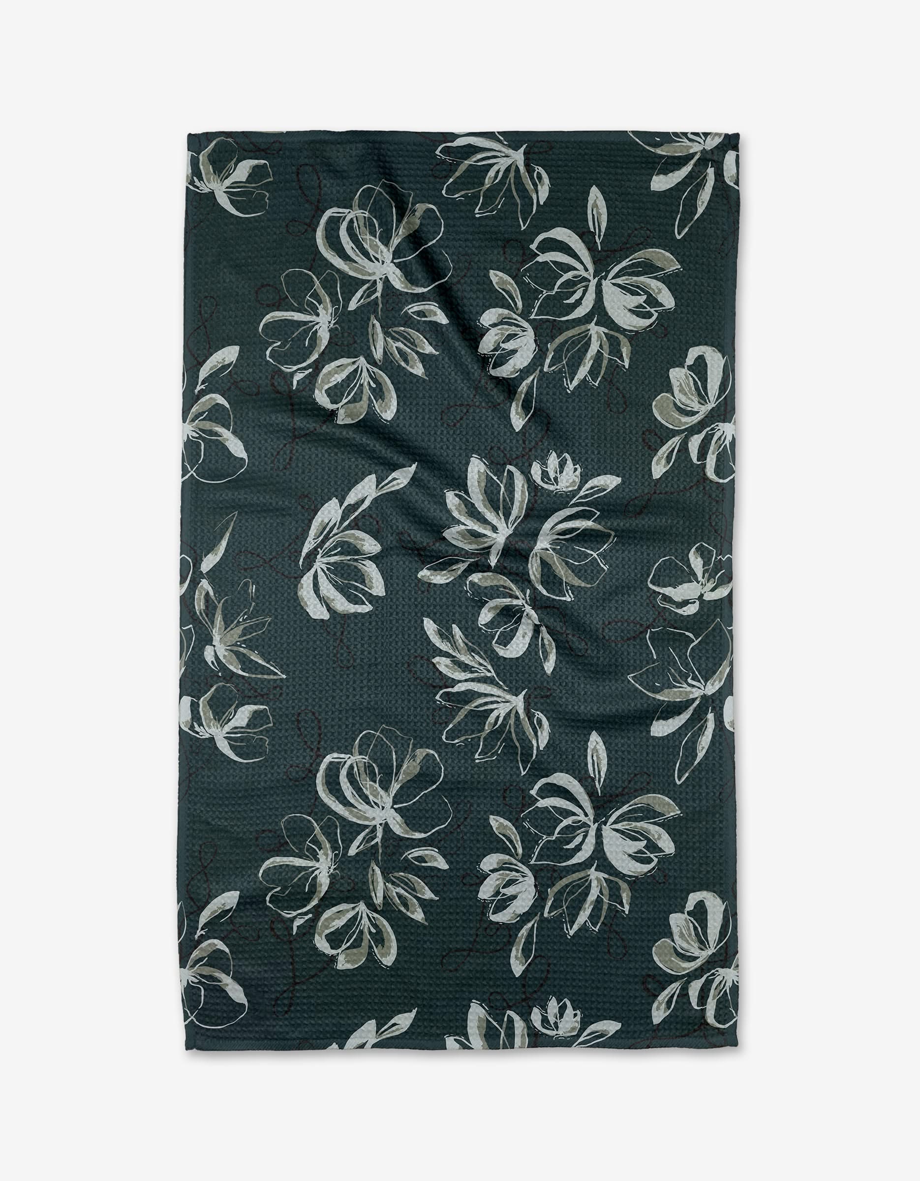 The Cherish tea towel by Toboggan Avenue features large white and light gray floral designs on dark green Geoweave™ fabric, made with recycled materials.