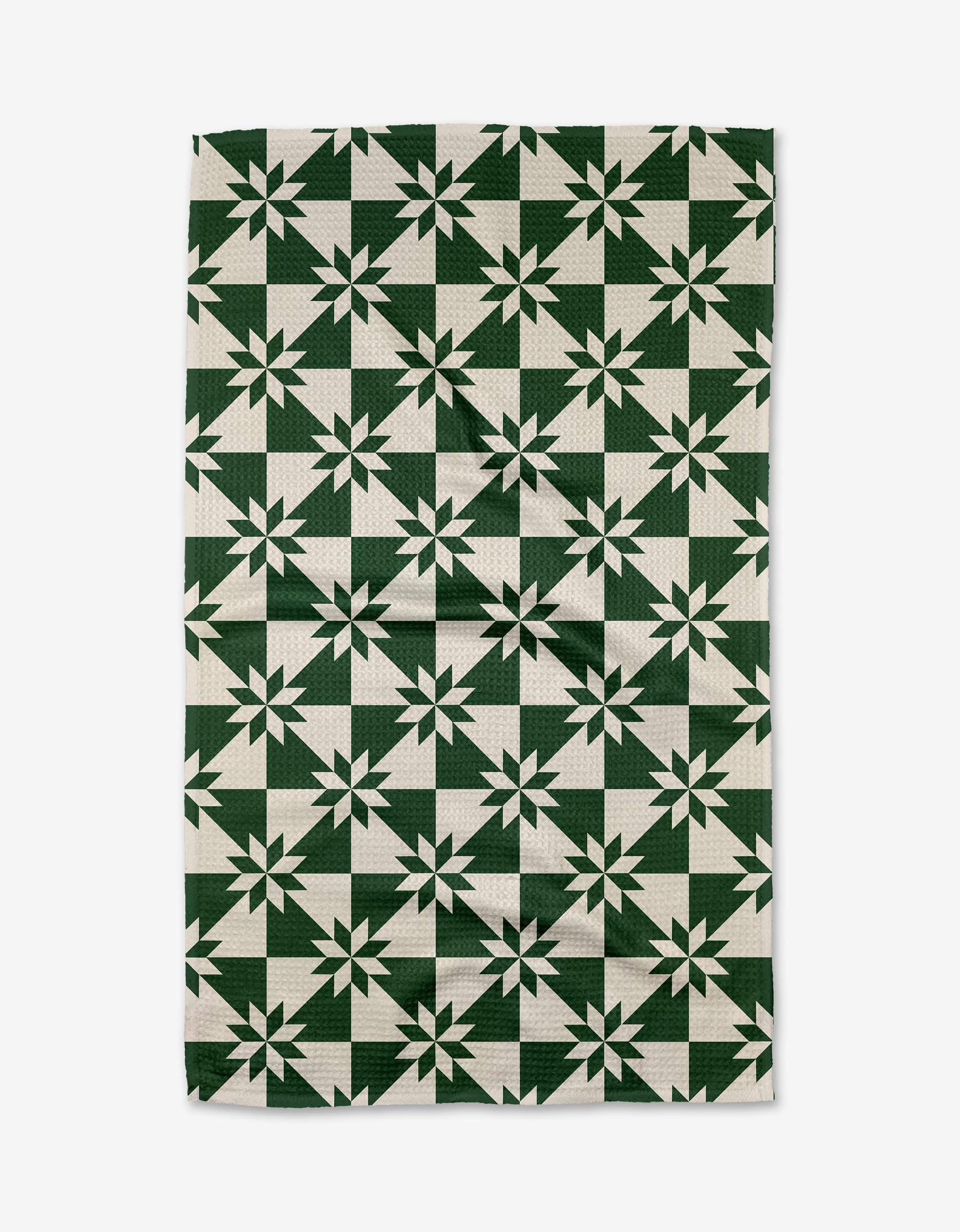 The Aubrey Fairchild Christmas Quilt Green is a rectangular tea towel with a dark green and white geometric star pattern, made from recycled materials for an eco-friendly, stylish touch to your kitchen.