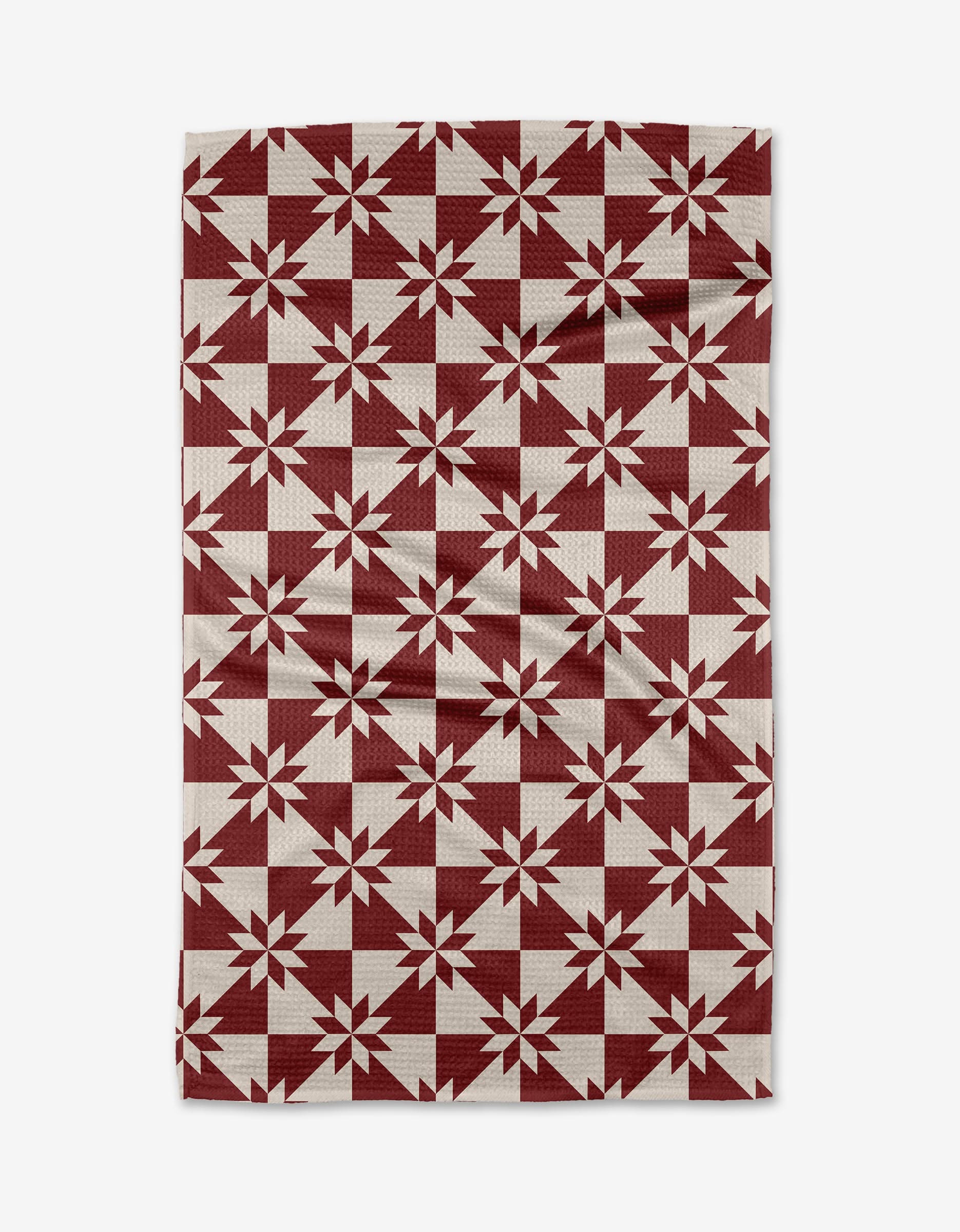 The Aubrey Fairchild Christmas Quilt Red kitchen towel features a burgundy and off-white geometric star pattern in a quilt style, crafted from recycled materials with a slightly wrinkled look.