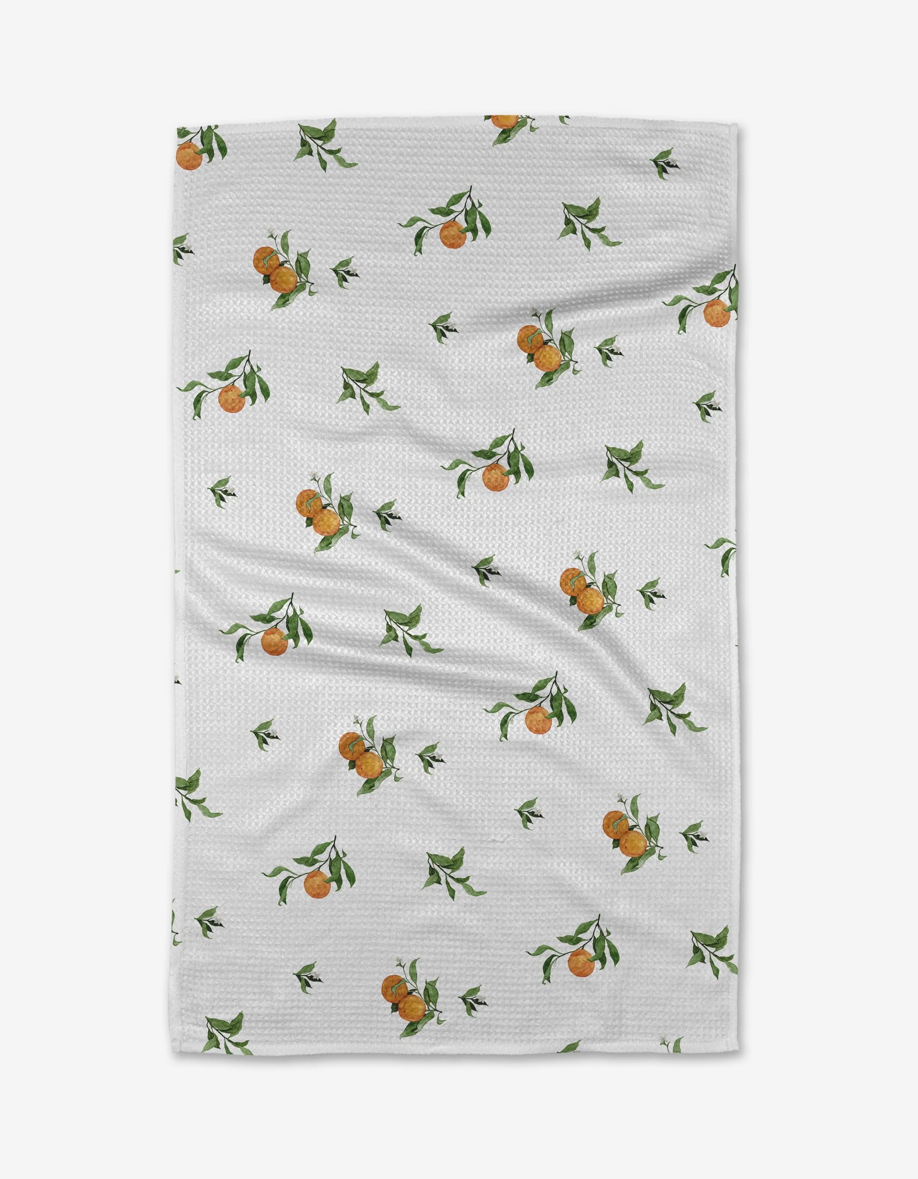 The Aubrey Fairchild Comfort Fruit tea towel, crafted from textured Geoweave fabric, displays small orange fruit clusters and green leaves on white. Slight creases are visible as it rests on a plain background.