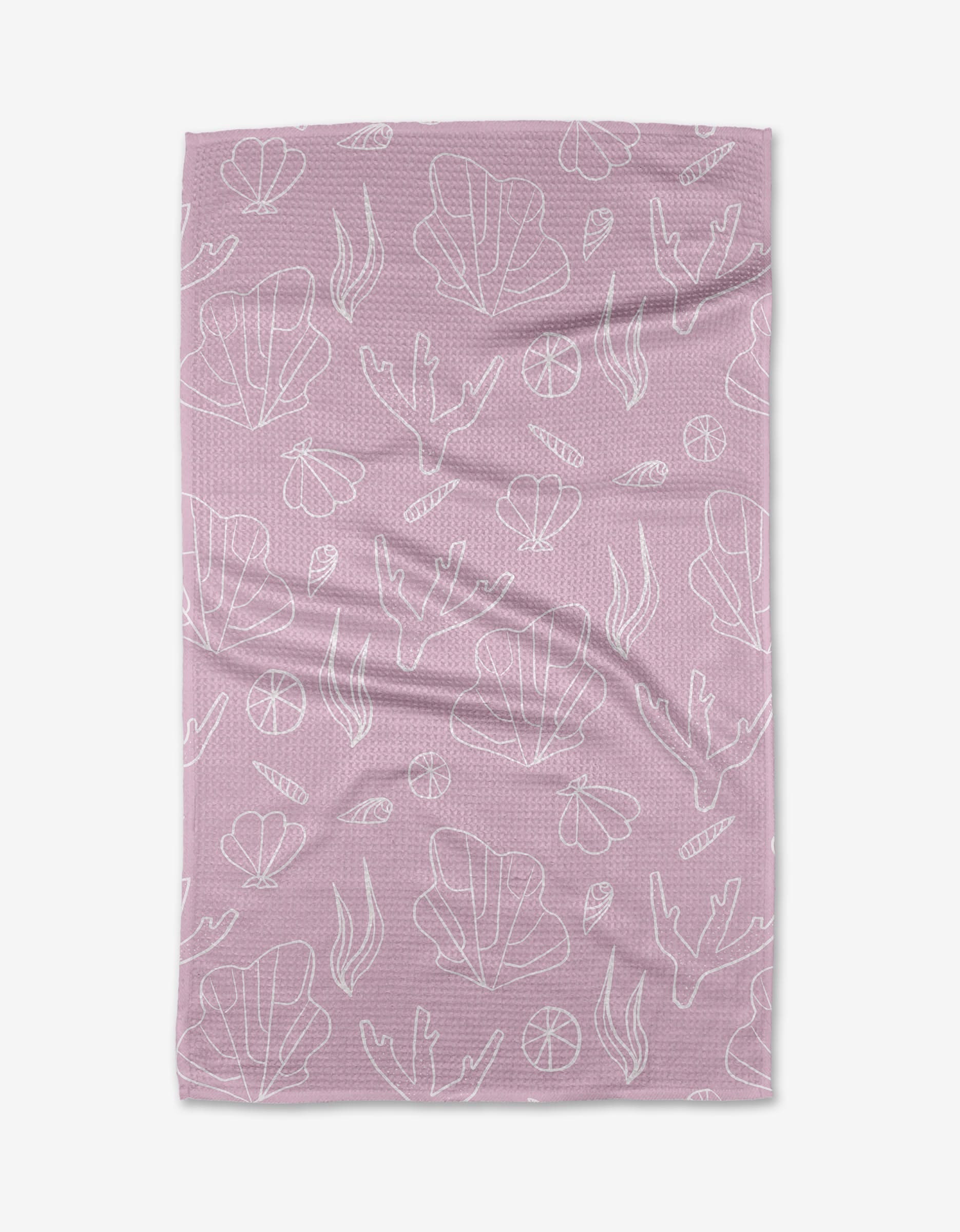 The Coral Cove tea towel by Janna Sue Design is mauve, made from recycled materials, and displays white line-drawn seaweed, coral, shells, and lemon slices scattered across its slightly wrinkled surface.