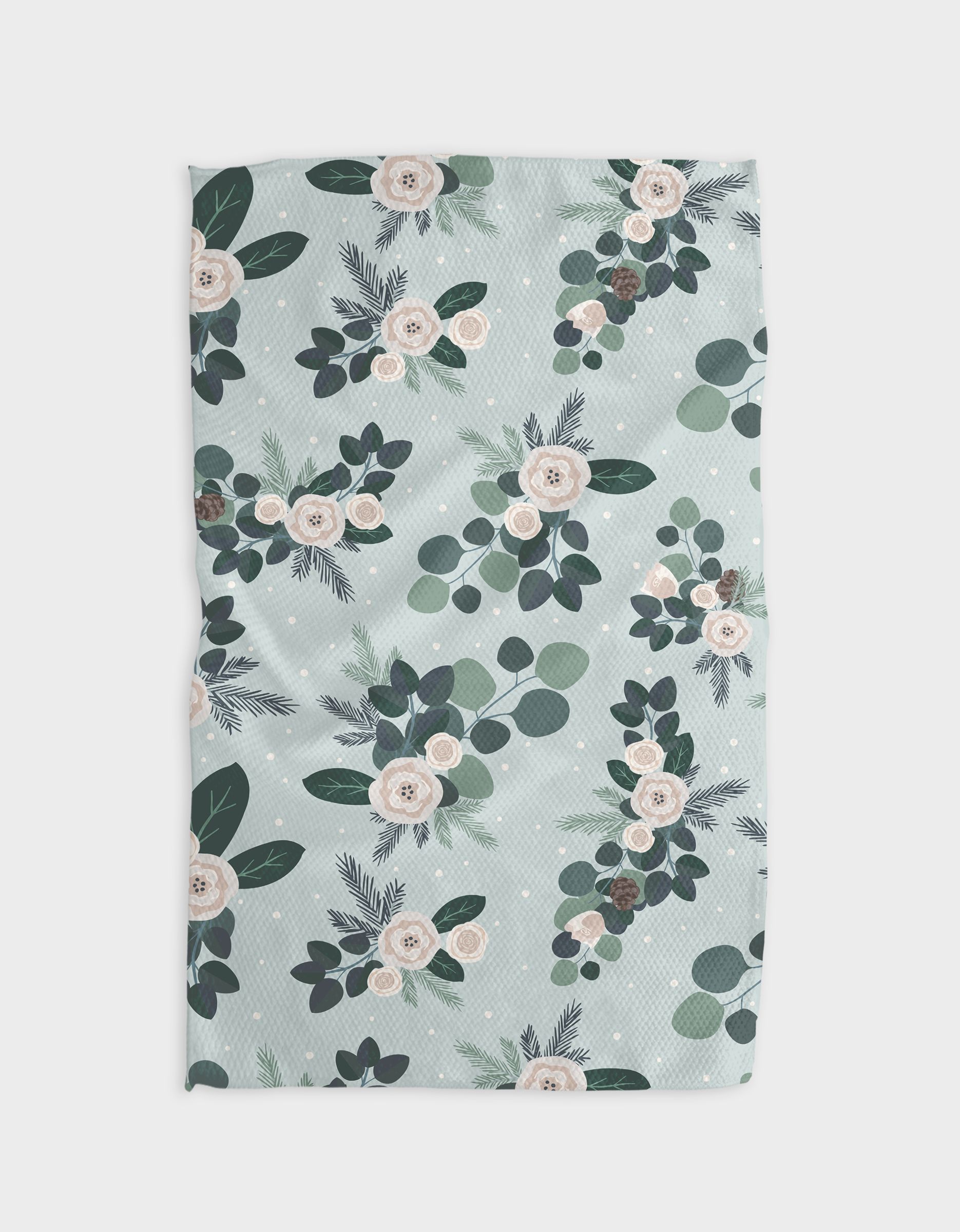 The GEOMETRY Country Winter blanket features soft blue-green Geoweave fabric with white and blush pink florals, dark green leaves, eucalyptus sprigs, and pine branches clustered on a dotted background.