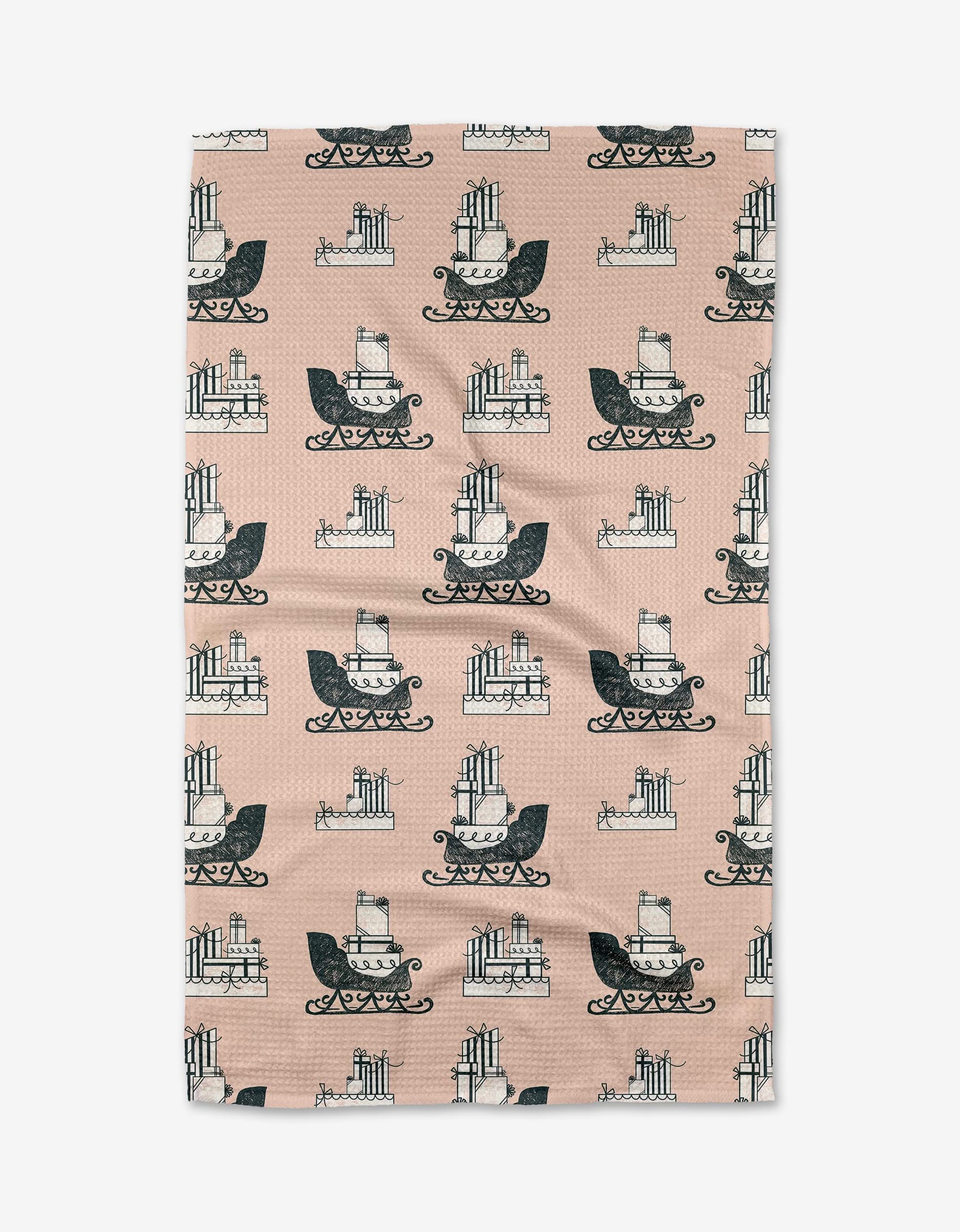 The Dashing Through the Snow pink kitchen towel by Charlie Rowan Designs is made from recycled materials and features a repeating black-and-white layered cake pattern with ornate scrollwork.