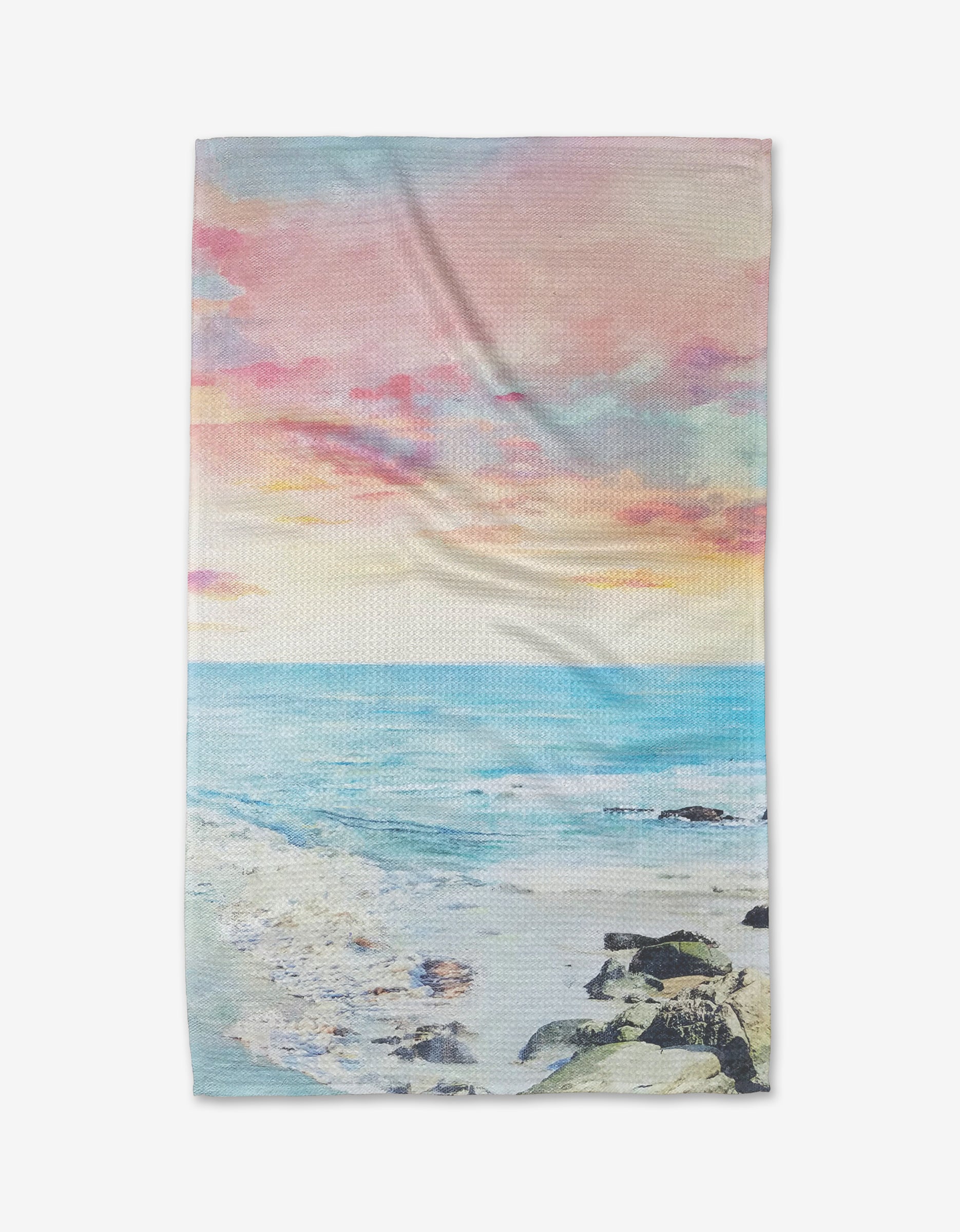 The “Epiphany” tea towel by Stefanie Bales features a serene beach scene with gentle waves, rocks, and a vibrant pink, orange, and blue sky at sunset or sunrise, crafted from soft geoweave fabric.