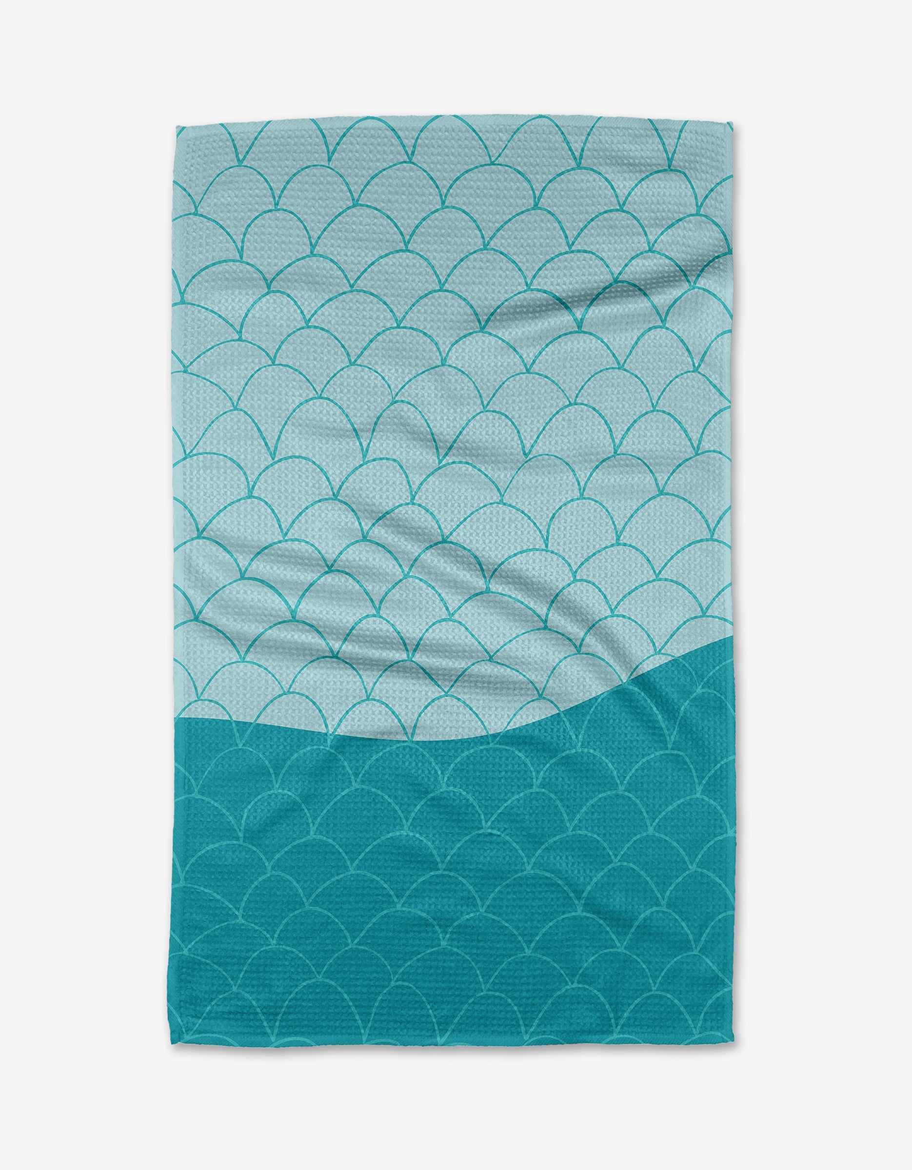 The Fish Scales tea towel by Marta Harvey is a rectangular towel made from recycled materials, boasting an overlapping blue and teal scallop design—darker teal at the bottom, lighter blue at the top.