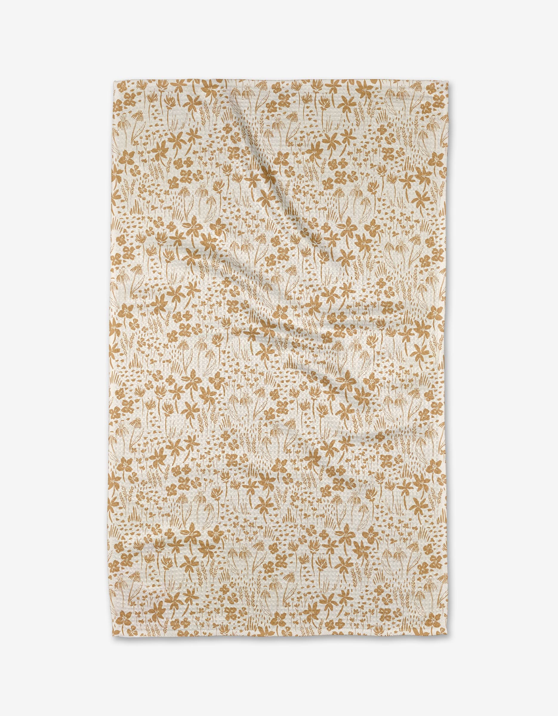 The Floating Meadow tea towel by Hufton Studio features an intricate golden brown floral pattern on beige Geoweave fabric, shown laid flat against a white background.