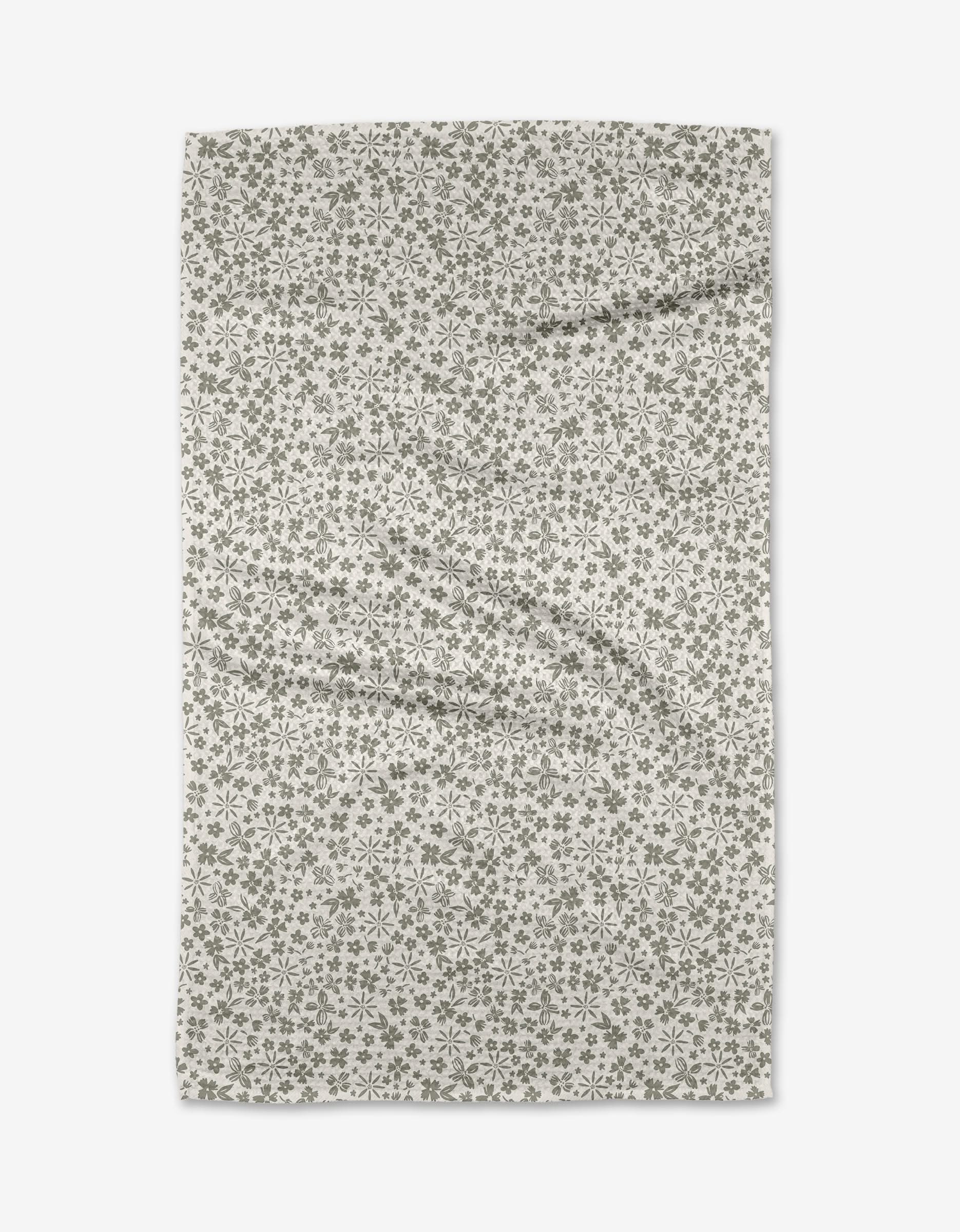 The Flourish Gardens tea towel by Hufton Studio features a rectangular beige Geoweave fabric with a small, repeating green floral pattern, displayed flat on a white background with subtle folds and wrinkles.