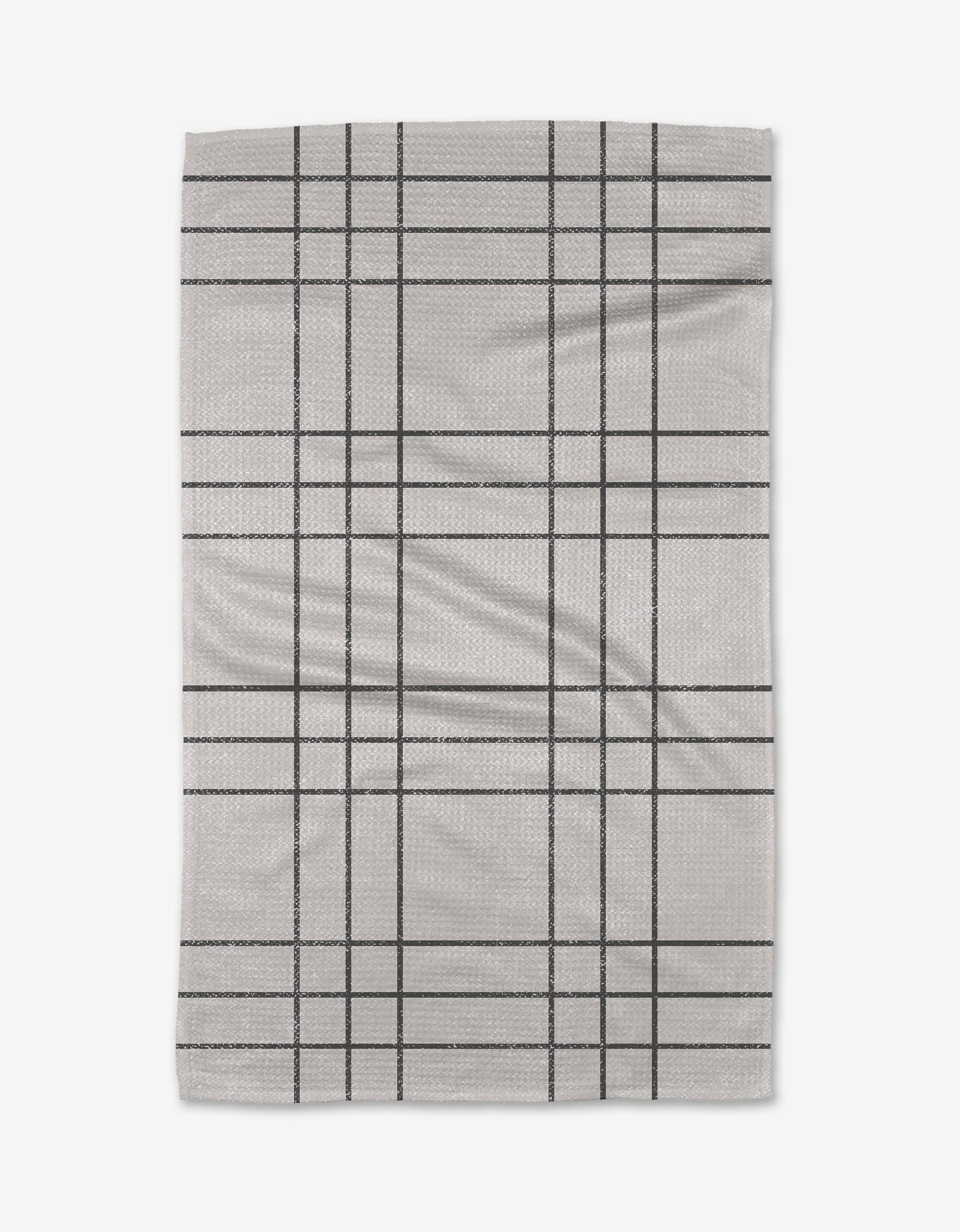 The Becki Owens Frosty tea towel features a light gray color with a simple black grid pattern, crafted from ultra-absorbent recycled materials, and is shown flat on a white background.