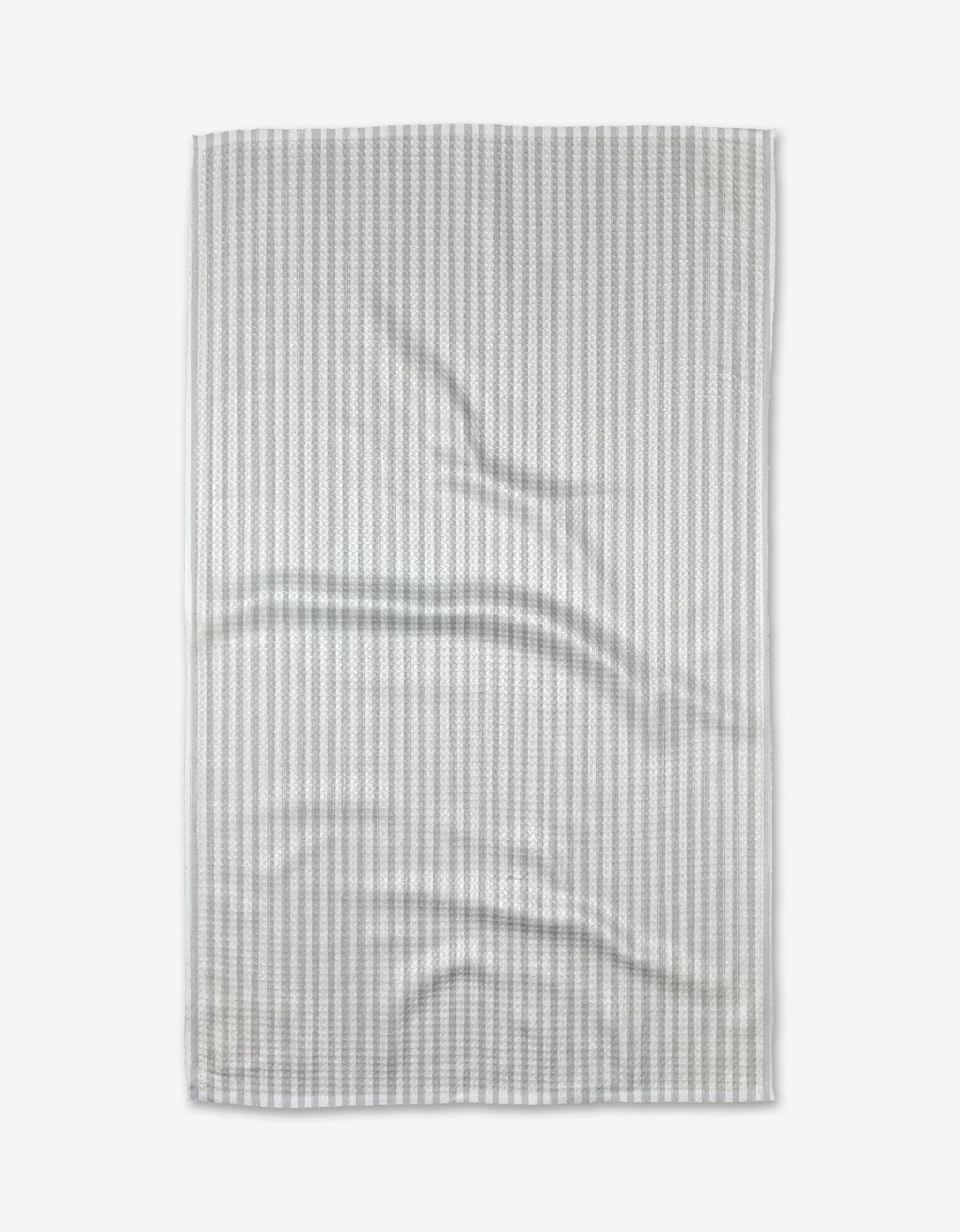 A Grey Salt tea towel by Kailee Wright is laid flat on a white background, showing light gray and white stripes with gentle folds across its ultra-absorbent Geoweave™ fabric.