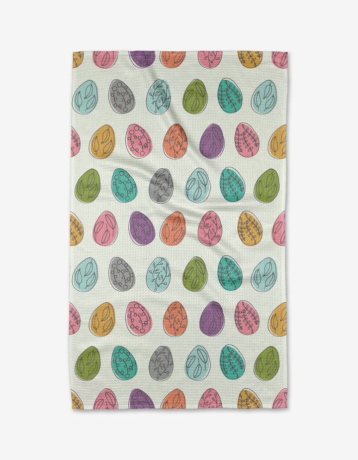 The Happy Go Lucky Eggs tea towel by Lizzie Clark features ultra-absorbent Geoweave fabric and a playful pattern of colorful, hand-drawn Easter eggs in pink, orange, yellow, green, purple, and gray on a white background.