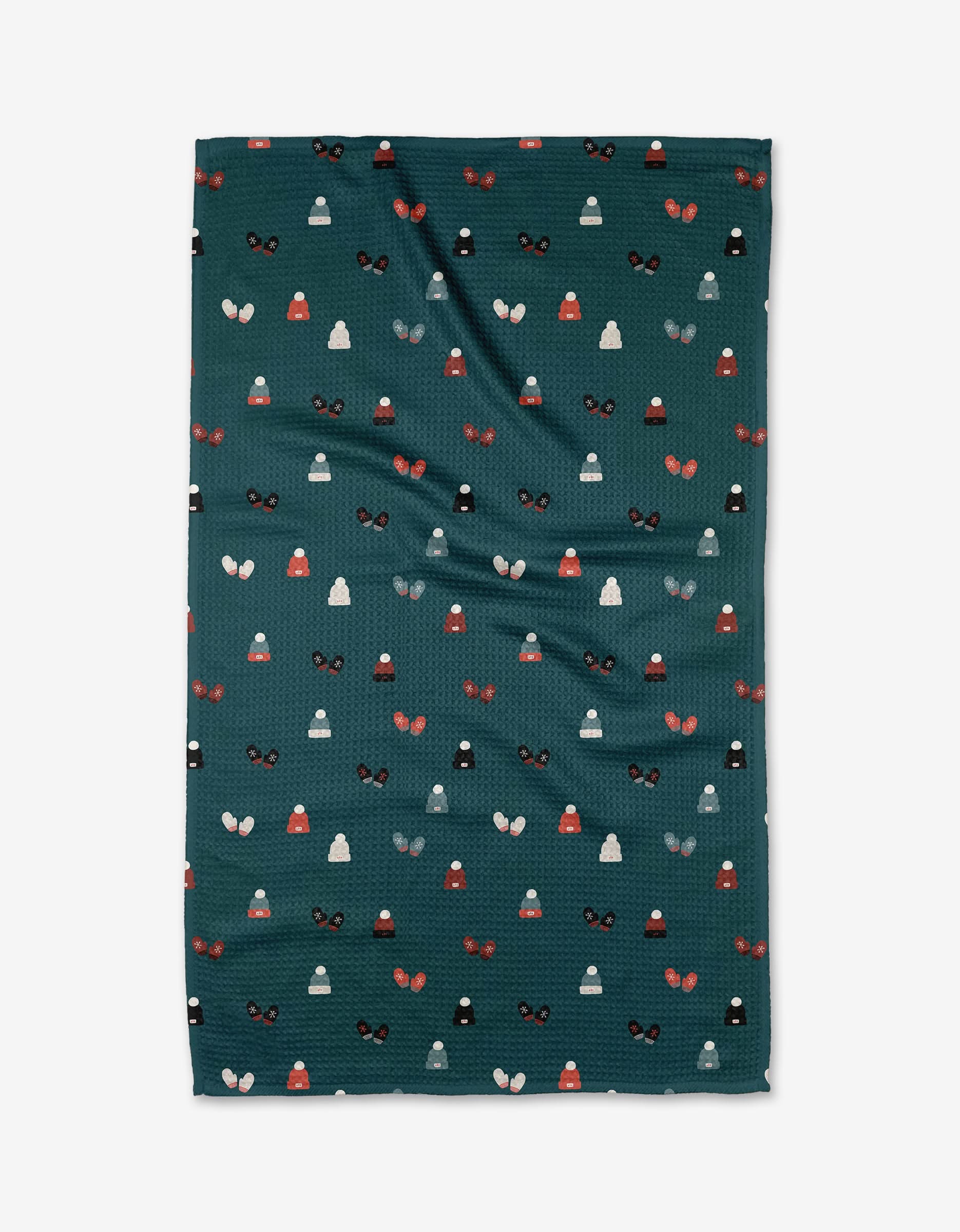 The Coit Creative Hats and Mittens kitchen towel is dark green, made from recycled material, and features a repeating pattern of small stylized winter hats and mittens in red, white, gray, and black.