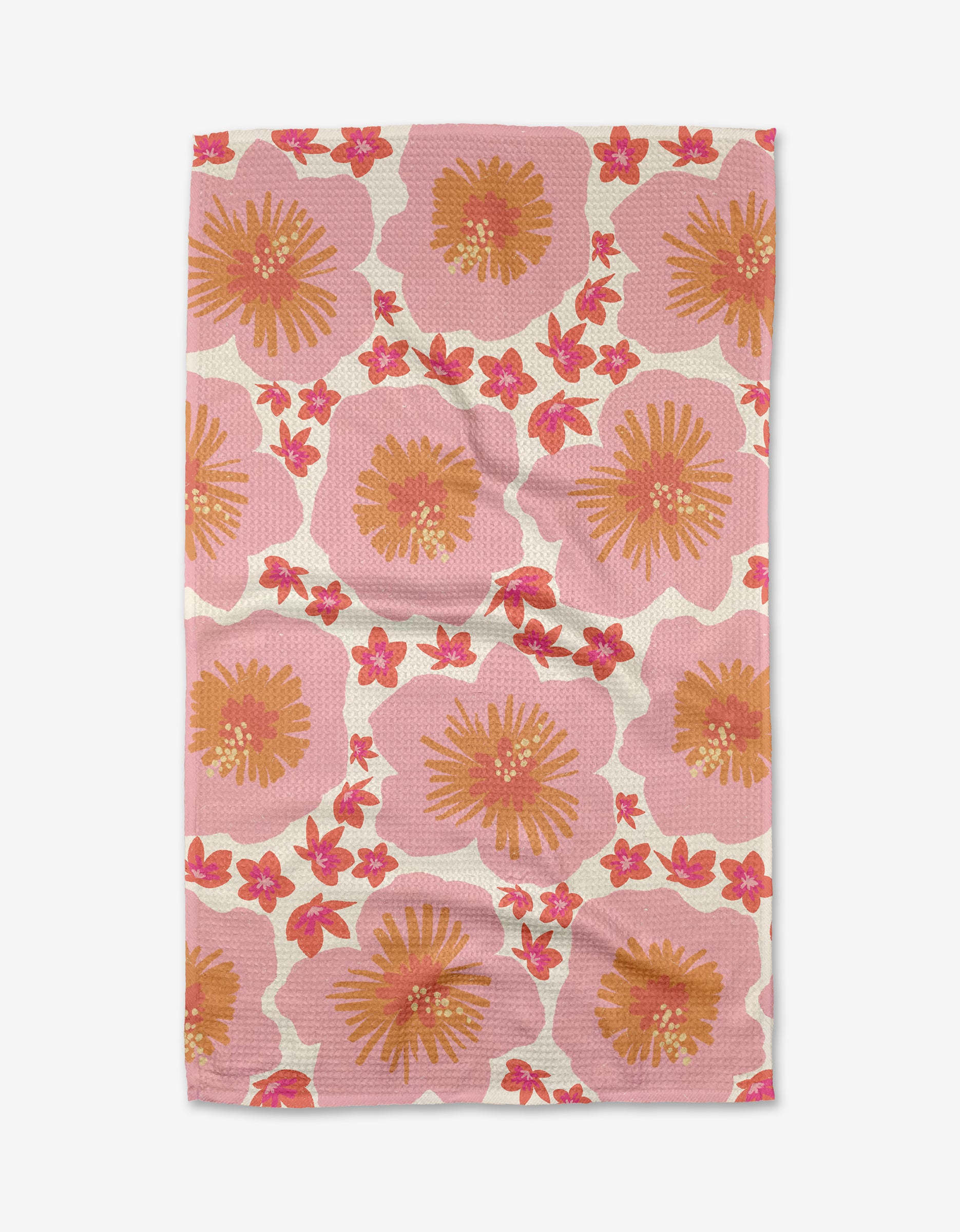 The “Hibiscus Sunset” tea towel by Janna Sue Design is rectangular, made from recycled material, and features a pink background with bold orange and yellow flowers plus smaller red blooms. The towel displays visible creases.