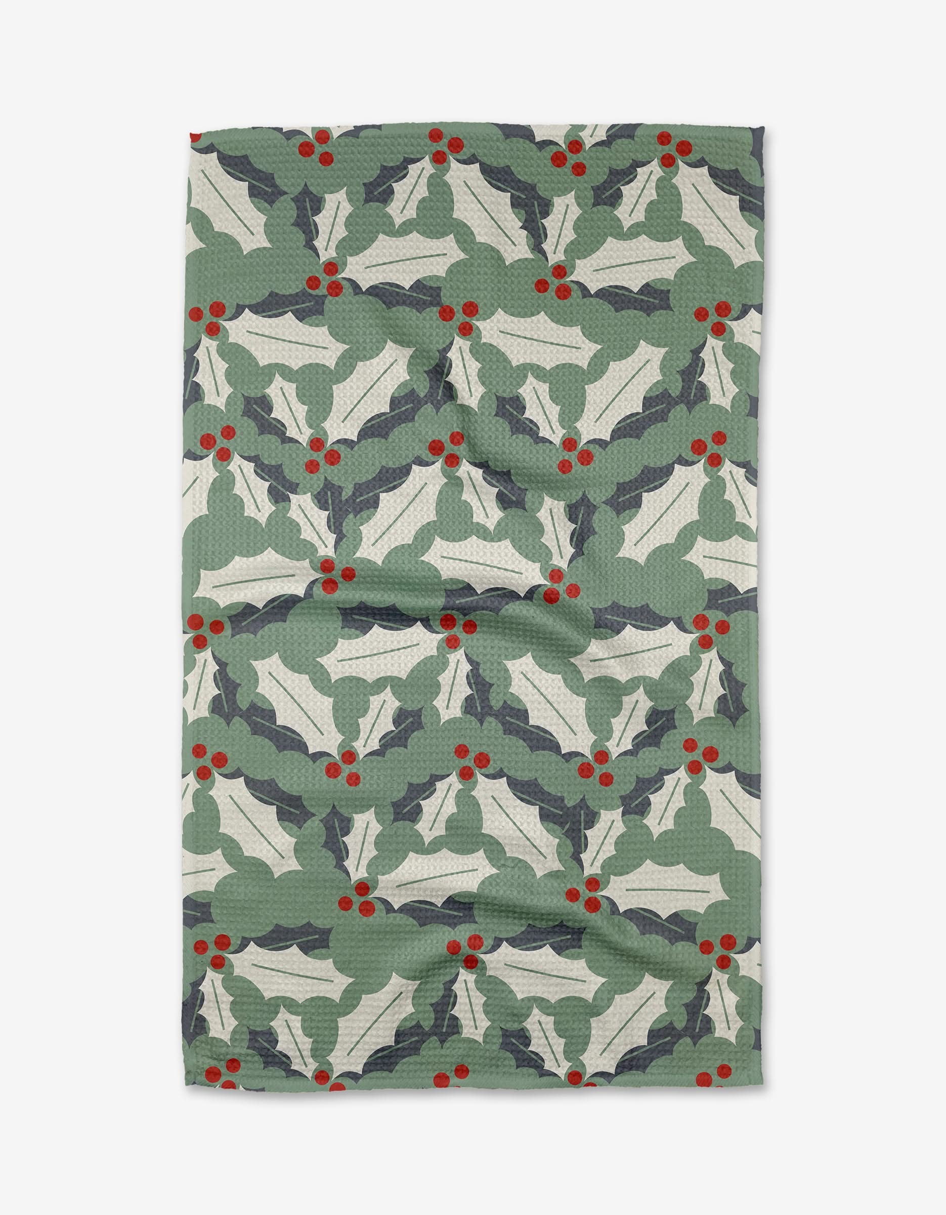 The Holly Jolly tea towel by Lizzie Clark features a festive pattern of green holly leaves and red berries on a light background. Made from recycled materials, it is slightly wrinkled and shown flat.