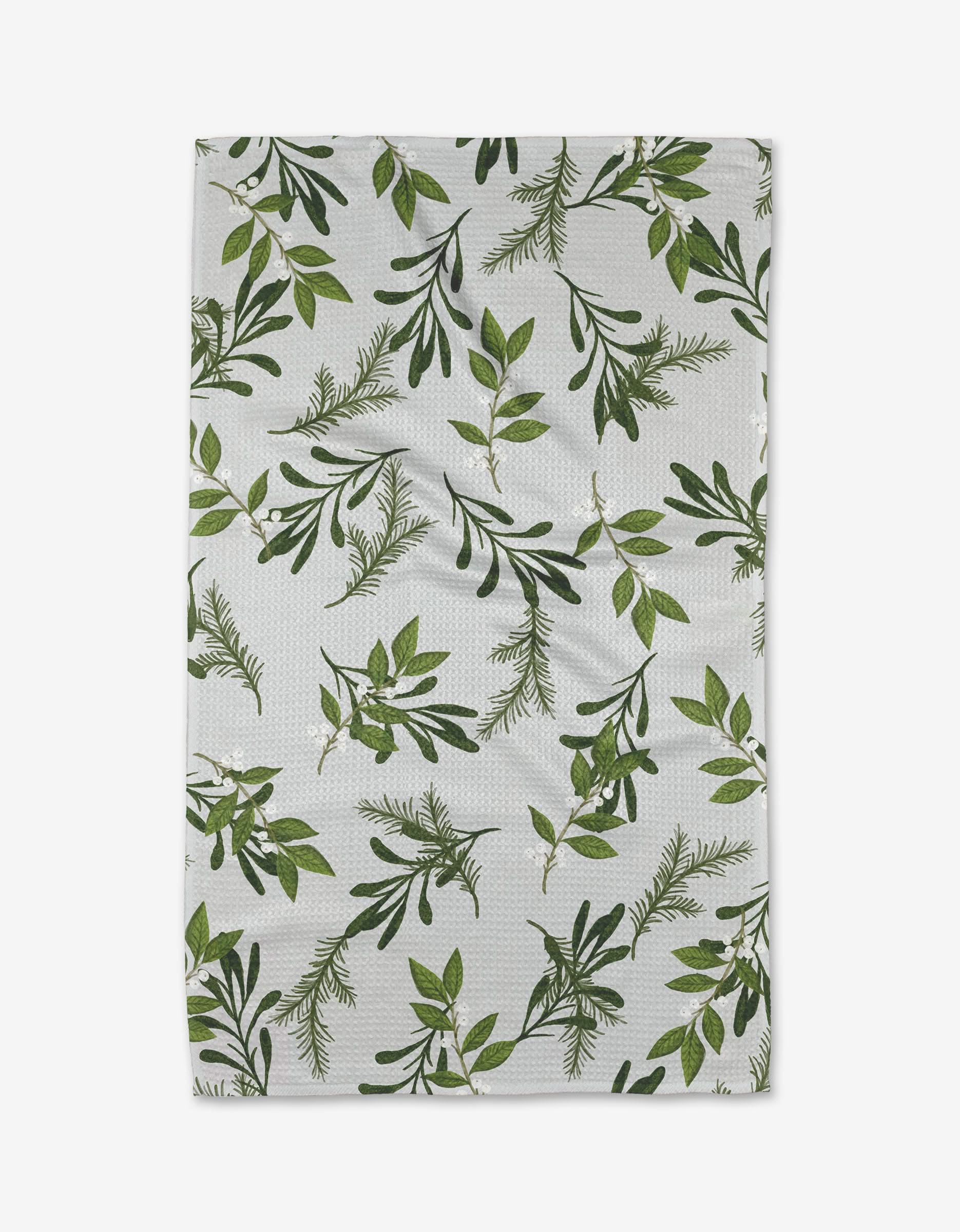 The Becki Owens Holly tea towel features a botanical design with green leaves and sprigs on white fabric, shown slightly wrinkled on a white background.