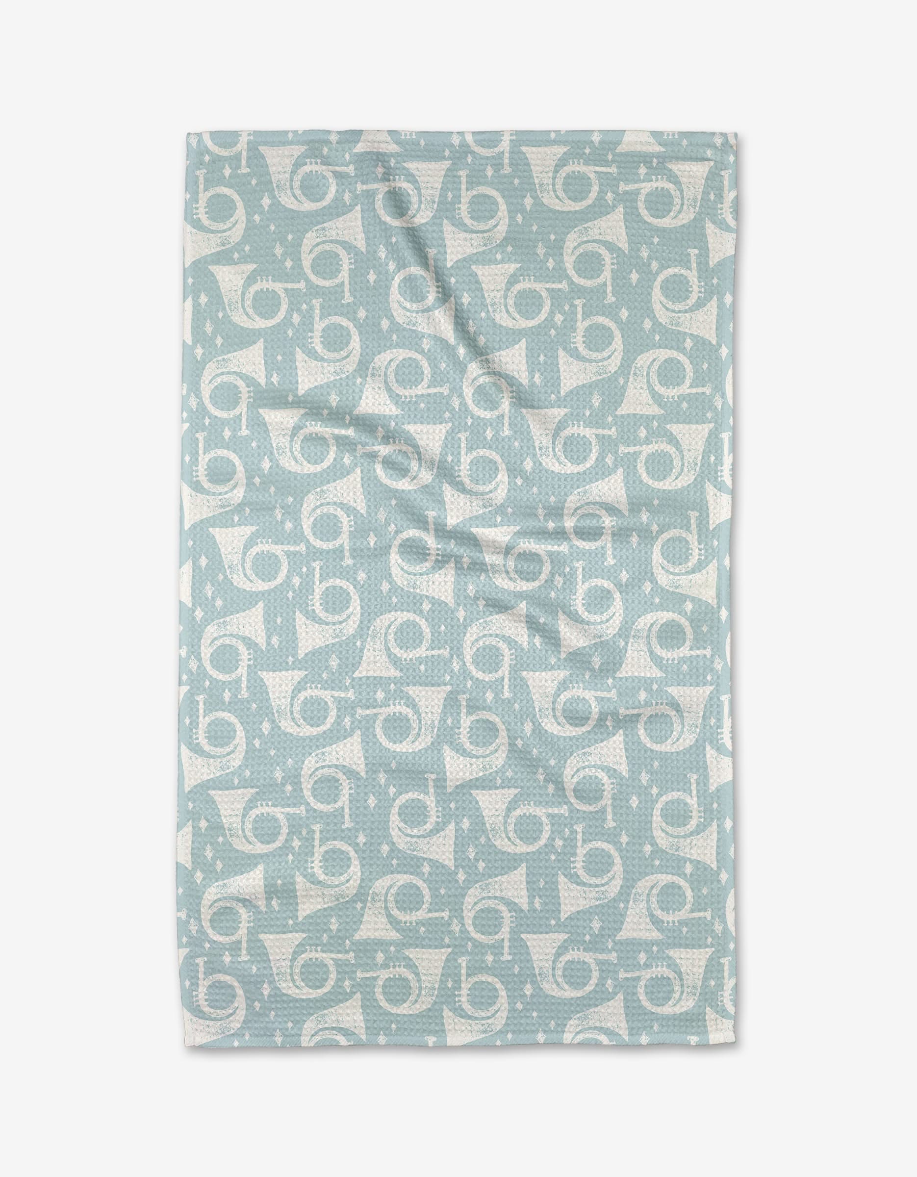 The Horns a Playing tea towel by Charlie Rowan Designs features light blue fabric with white geometric, swirl, dot, curved line, and star patterns. Made from recycled materials, this ultra-absorbent towel is shown laid flat with slight wrinkles visible.