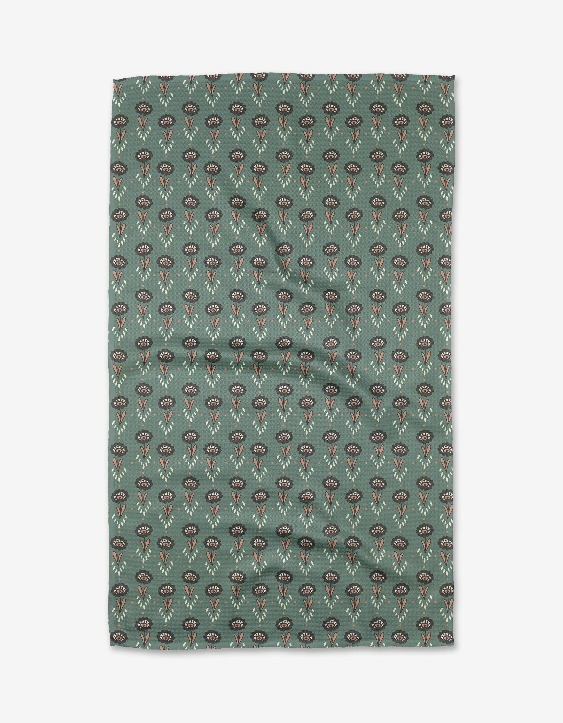 The Jungle Petals tea towel by Amita Nair features green Geoweave fabric with a pattern of small, stylized red, black, and beige flowers, shown flat with slight wrinkles.