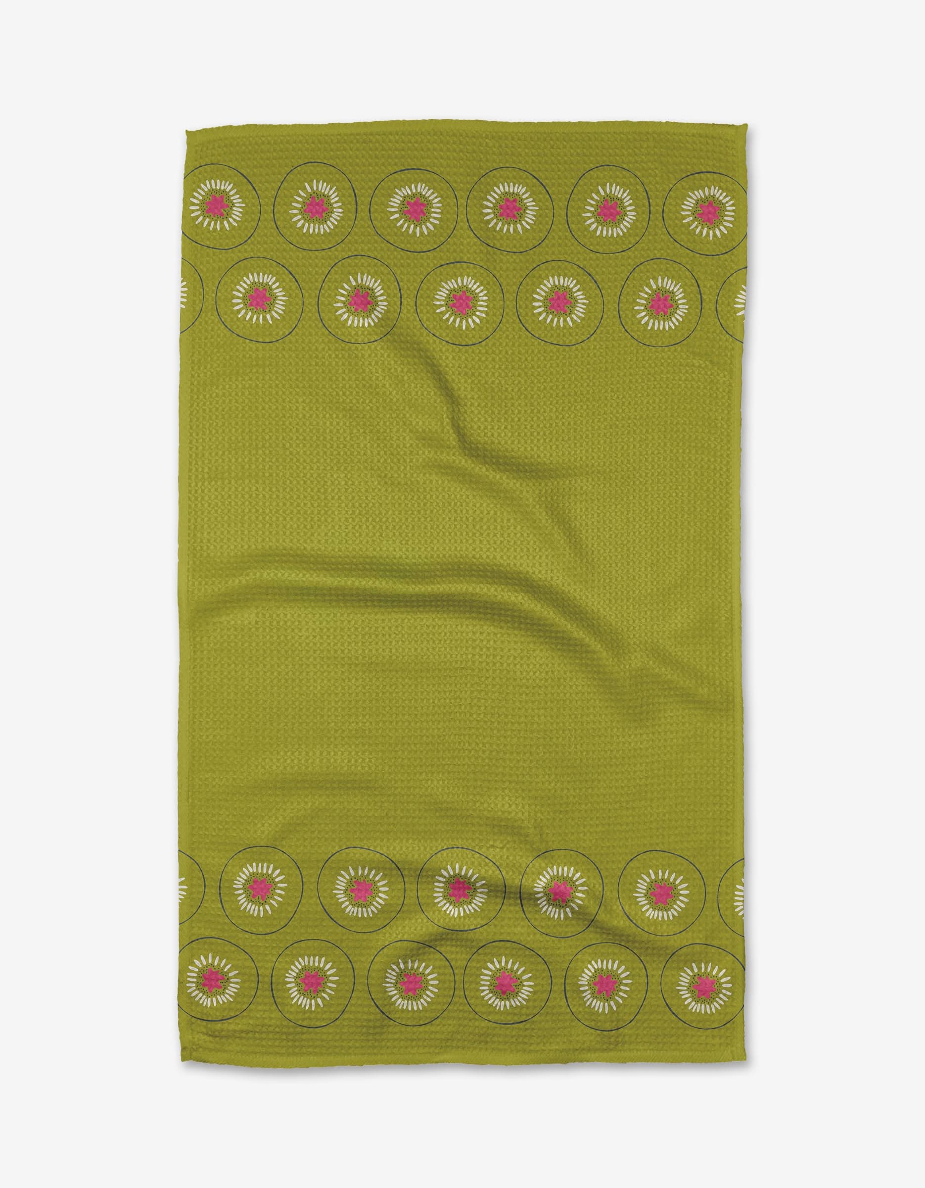 The Kiwi Kraze tea towel by Lizzie Clark is green and rectangular, featuring red and white circular floral motifs on the top and bottom edges. Made from Geoweave™ fabric, it has a subtle textured grid background.