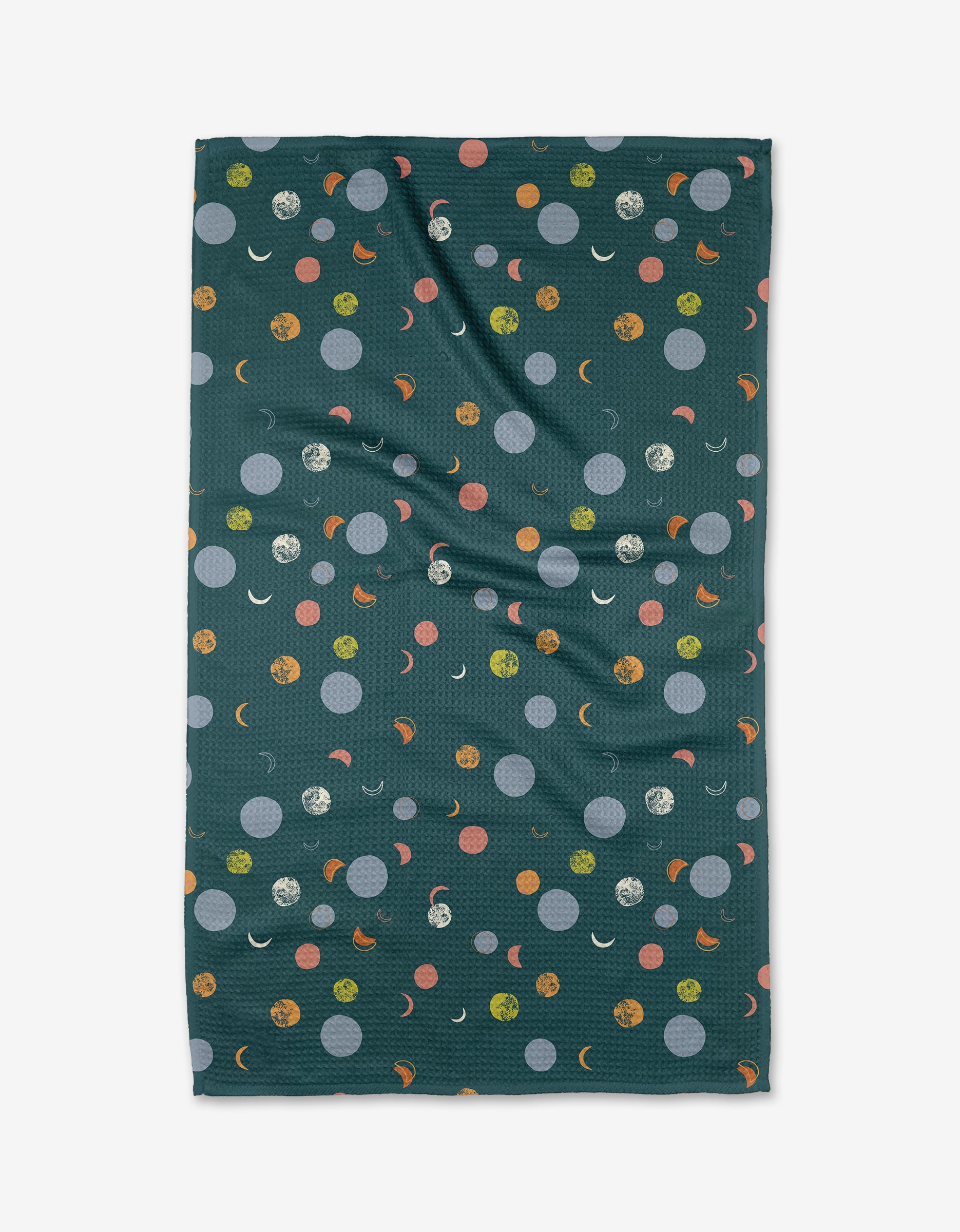 The Lumina kitchen towel by Jessica Swift is a dark green, rectangular towel with orange, yellow, blue, and white dots, crescent moons, and textured circles. Made with recycled materials; fabric has slight wrinkles. Photographed on a white background.