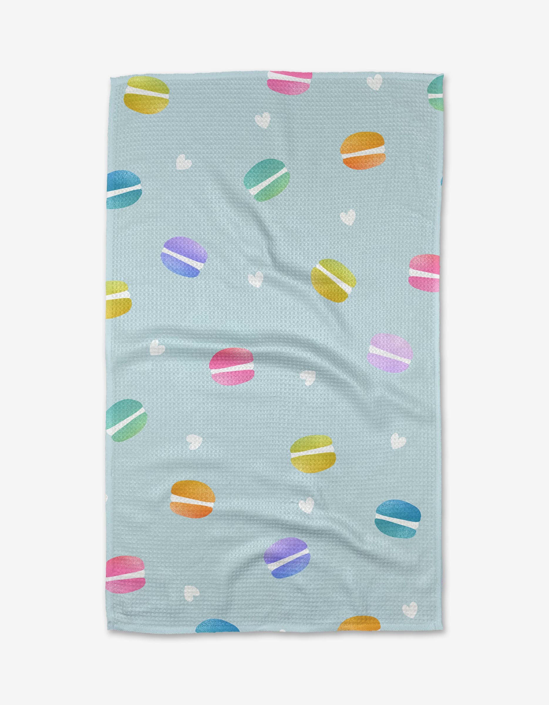 The Mac Flip by Noras Macarons is a light blue blanket featuring colorful macarons in pink, yellow, green, blue, and purple with white hearts on ultra-absorbent, eco-friendly Geoweave fabric.