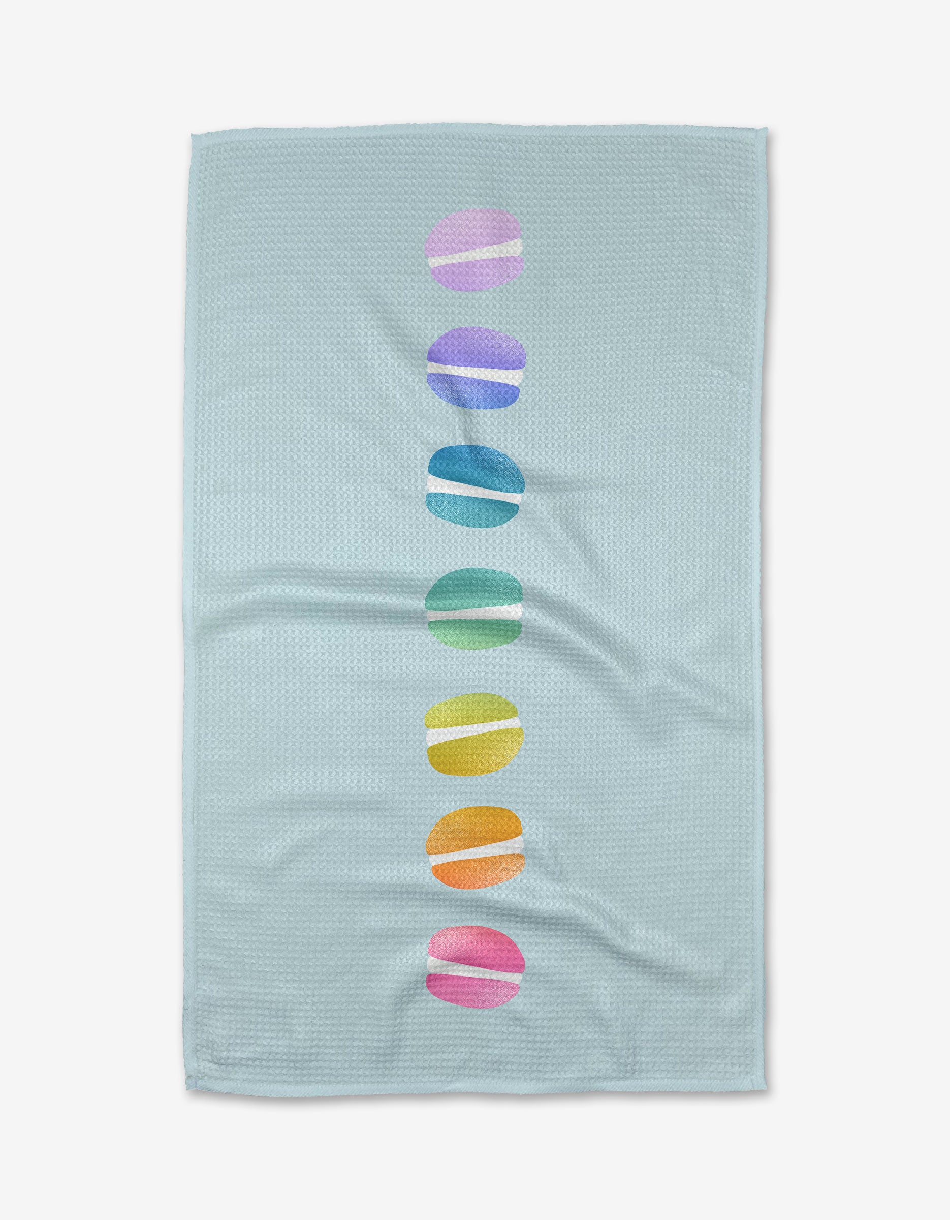 The Mac Love Kitchen Tea Towel by Noras Macarons features light blue Geoweave fabric with a centered vertical row of seven colorful, rainbow-hued macaron ovals.