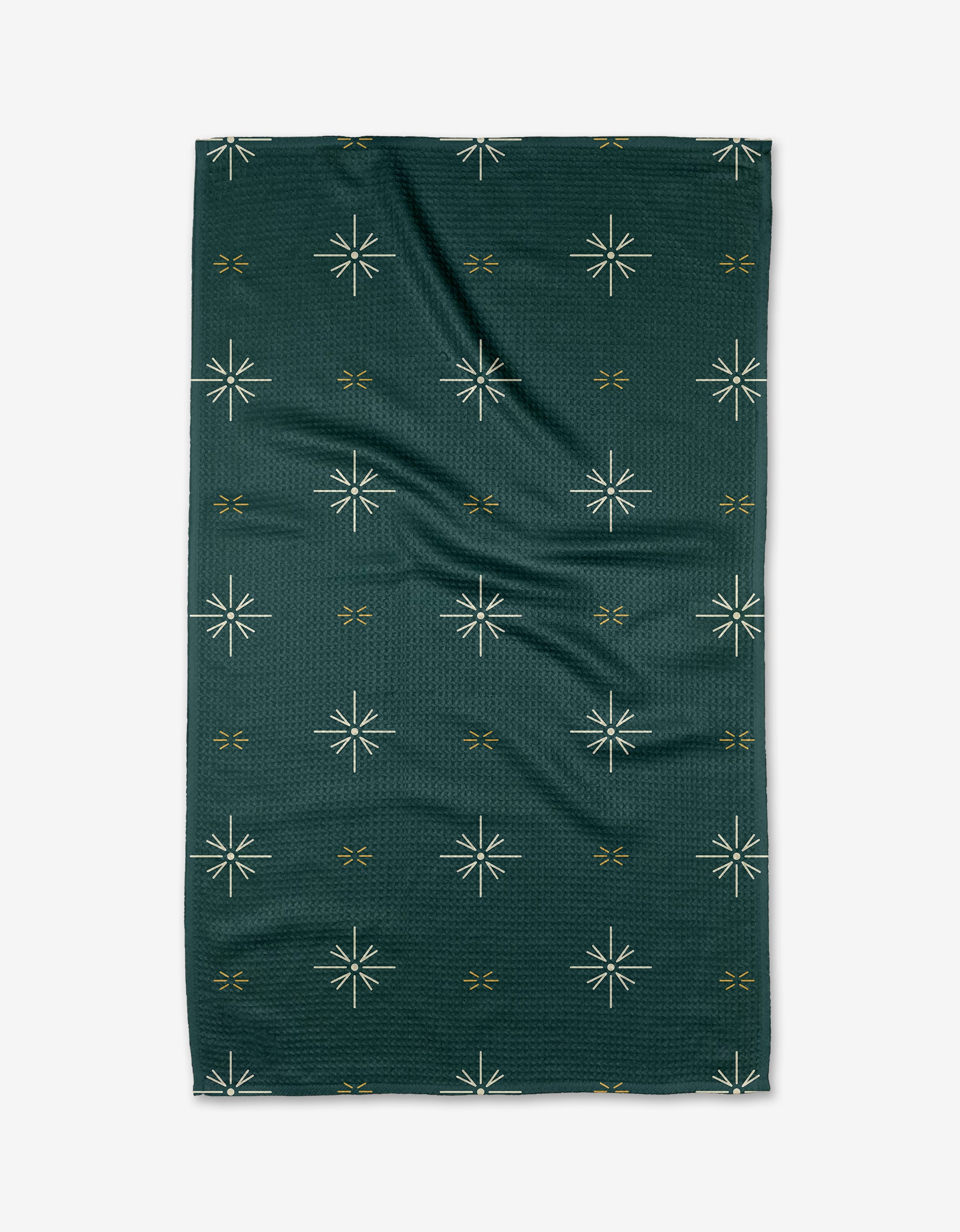 The Marine Navigation tea towel by Twig + Spark is a dark green rectangle with white starbursts and small gold x-shapes on a textured background. Quick-drying, it’s shown flat with slight creases.