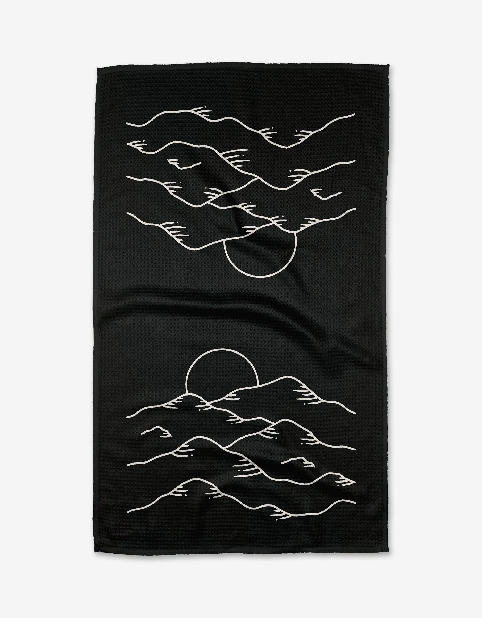 The Midnight Mountain Tea Towel by Graphics and Grain is black, made from Geoweave fabric, and showcases minimalist white line art of a sunset behind mountains and clouds, with the design repeated vertically.