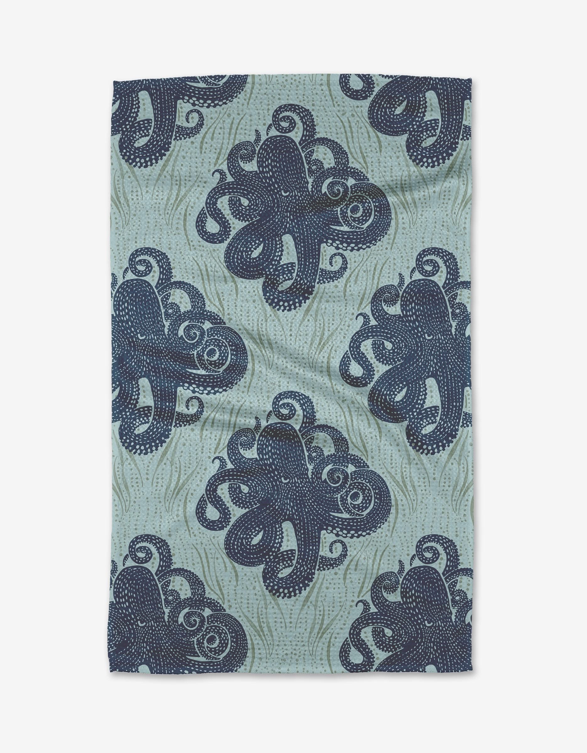 The Mighty Octopus tea towel by Katie OShea is rectangular and made from recycled materials, showcasing dark blue octopuses with swirling tentacles on a light blue wavy background.