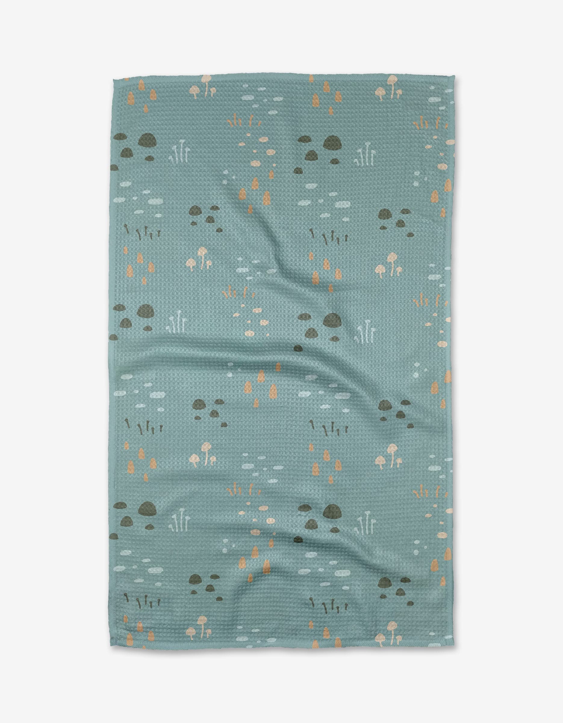 The Mini Shroom Sprouts kitchen towel by Amberleigh Adoff features a light blue, textured recycled fabric with a scattered pattern of small brown, beige, and orange mushrooms and grass on a white background.
